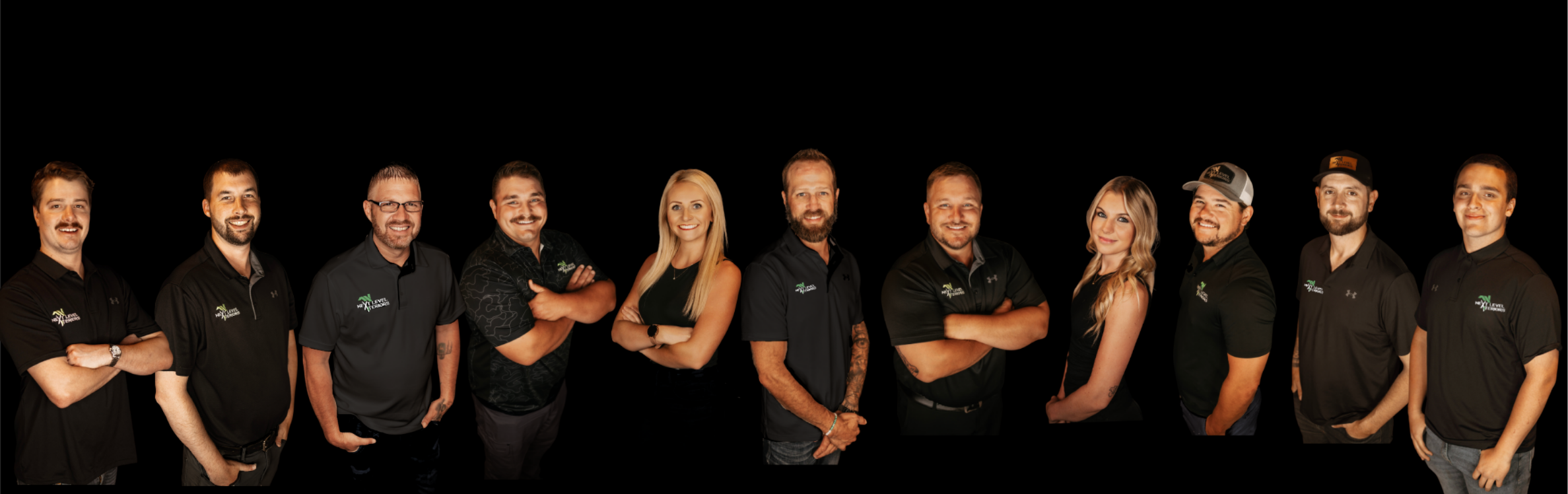 Group of eleven professionals standing in a row against a black background, wearing black shirts with a logo, smiling and posing confidently.