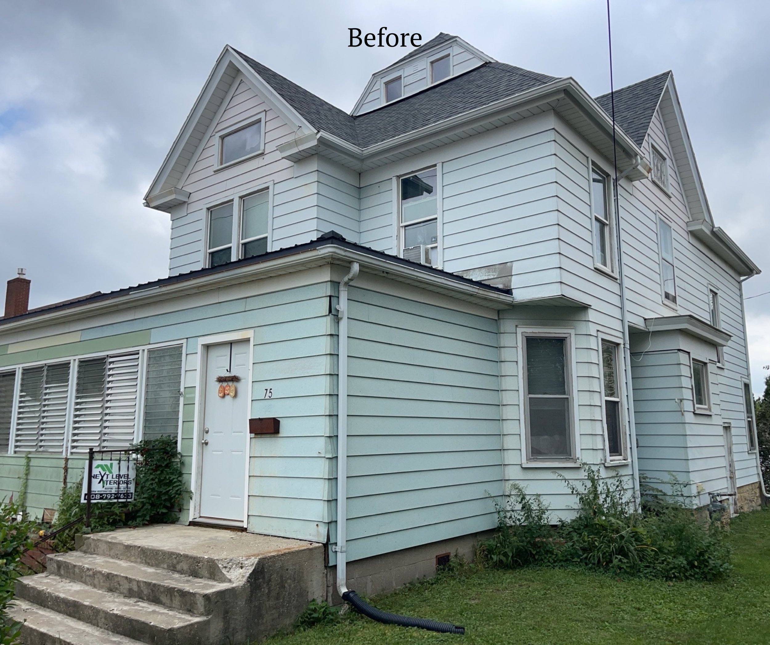 A light blue multi-story house with white siding and several windows. The front entrance has concrete steps, a white door, a black mailbox, and a sign that reads "Next Level." Overcast sky in the background.