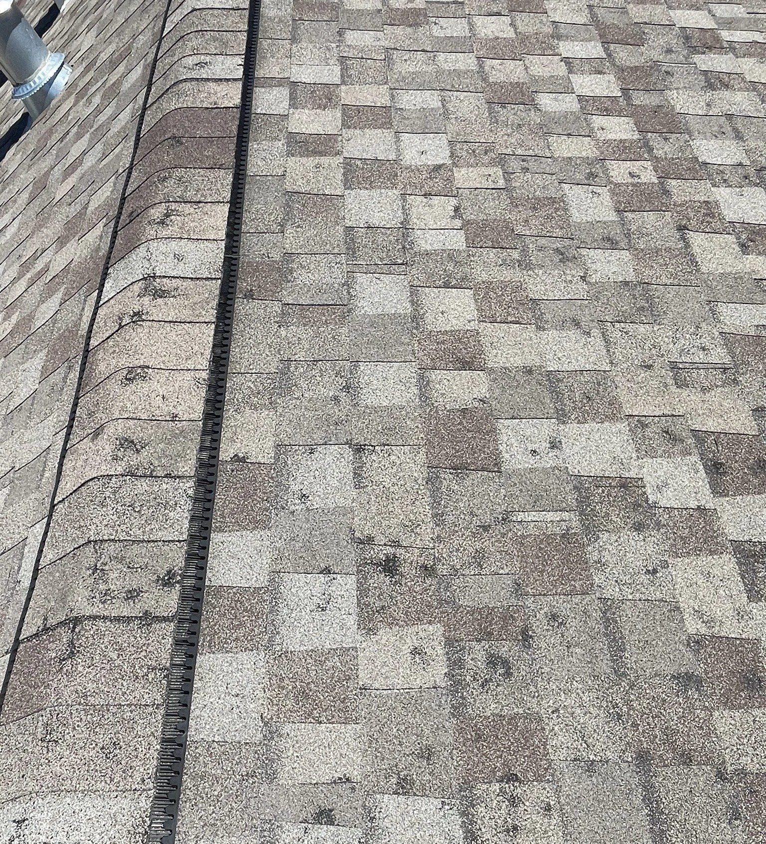 Gray and brown asphalt shingle roof with a black object laid across it and a gray vent pipe on the side.