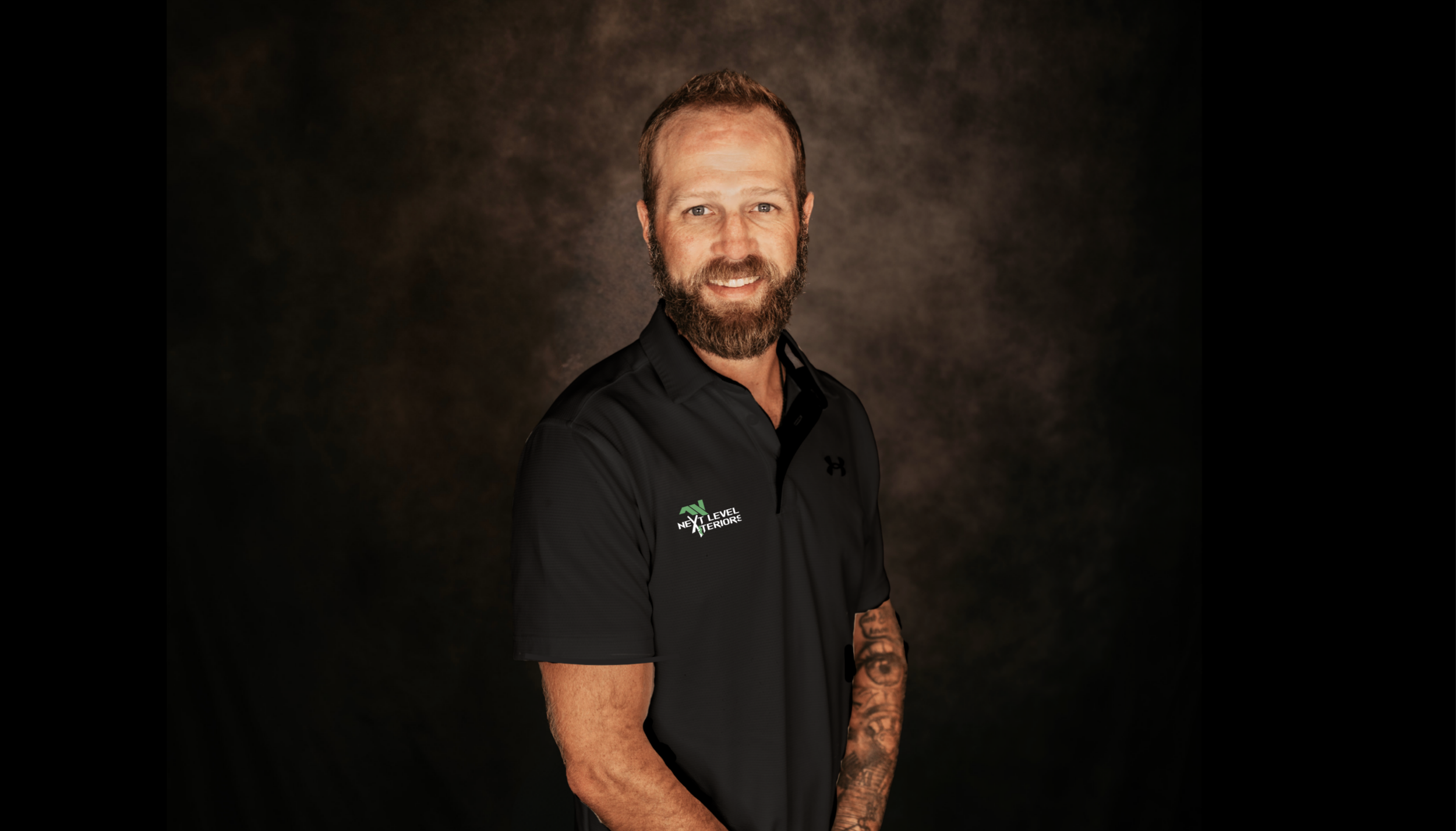 A man with a beard and short hair smiling at the camera, wearing a black polo shirt with a logo that reads 'Next Level Interiors'.