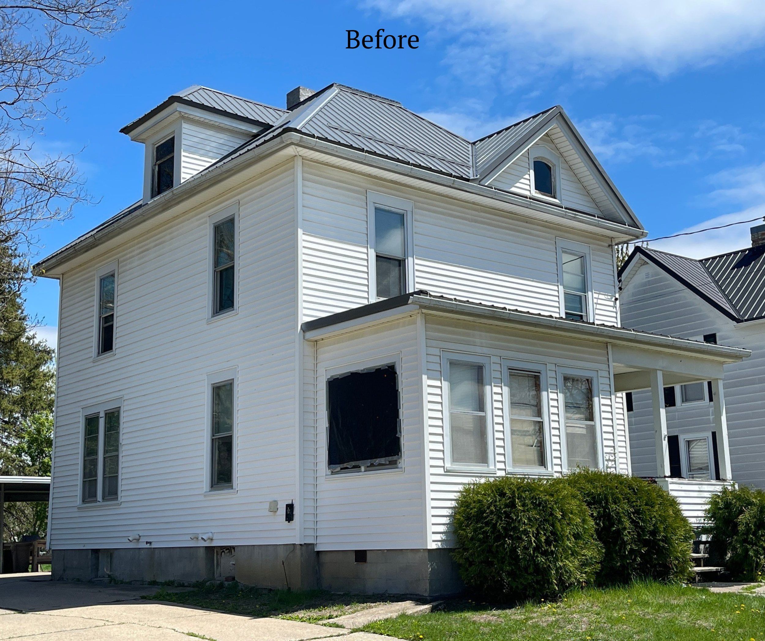 White three-story house with a gabled roof, multiple windows, and a porch, surrounded by greenery and under a partly cloudy sky.