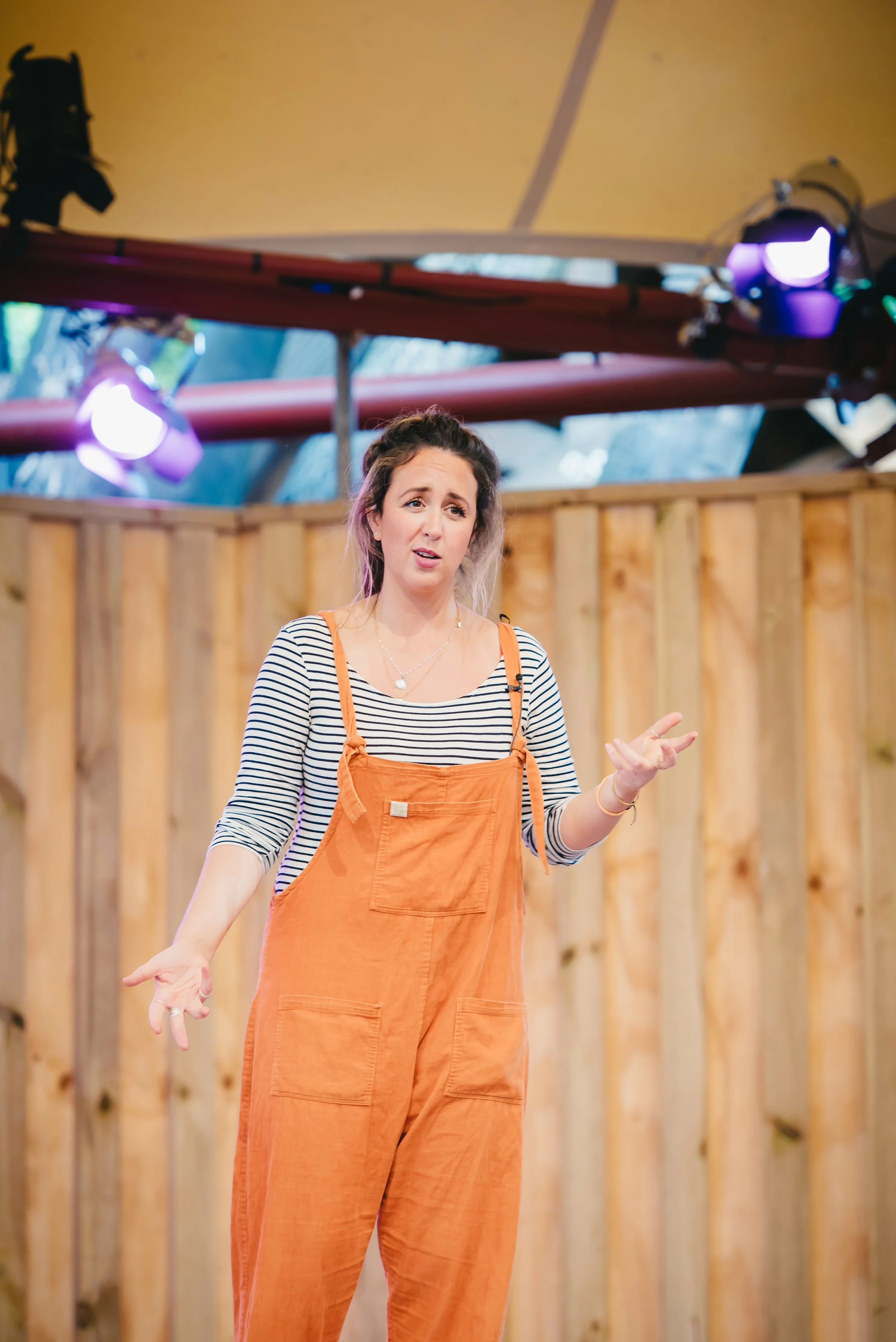 Roann Hassani McCloskey is wearing an orange jumper with black and white striped long sleeve shirt and performs at Globe Theatre