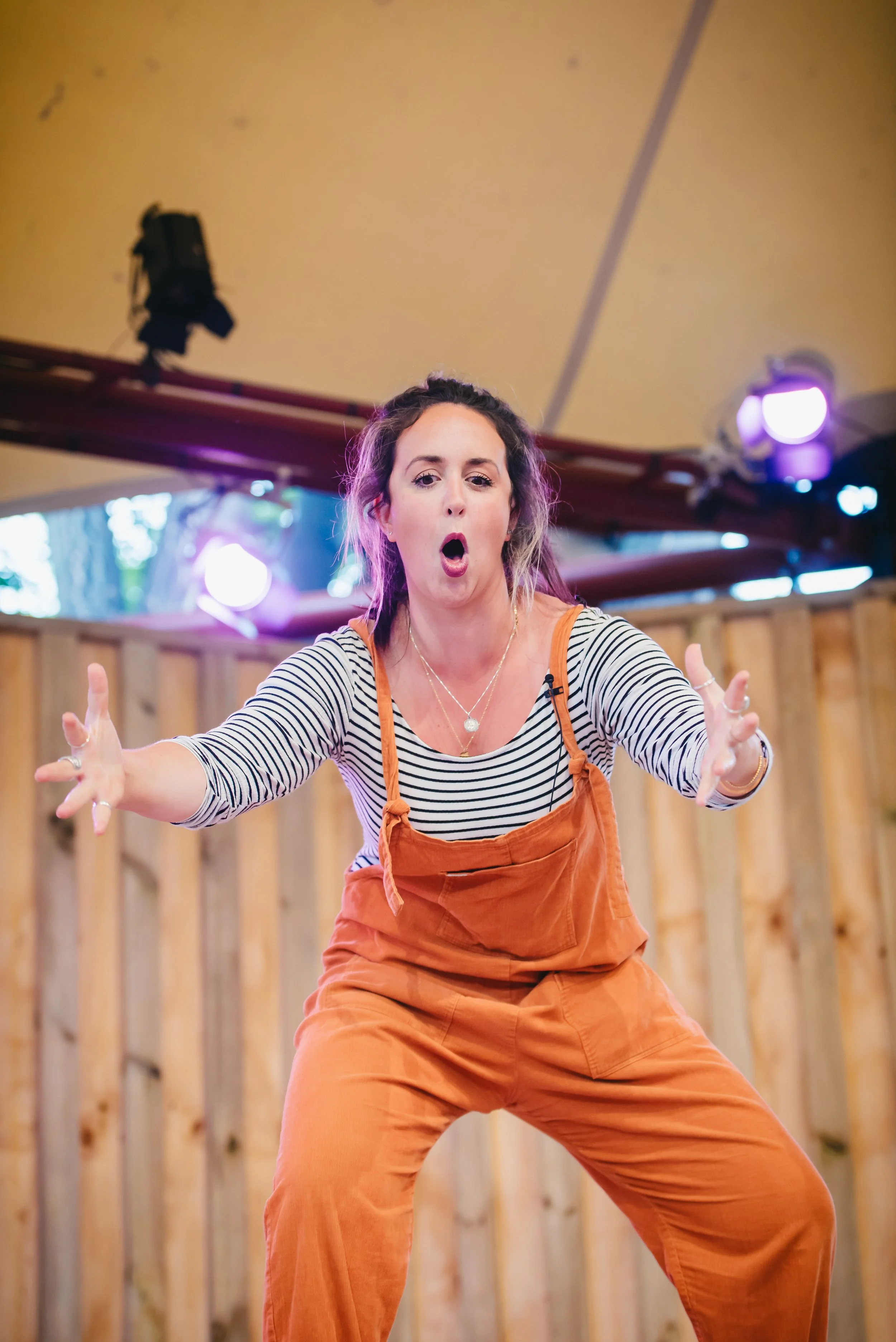 Roann Hassani McCloskey is wearing an orange jumper with black and white striped long sleeve shirt and performs at Globe Theatre