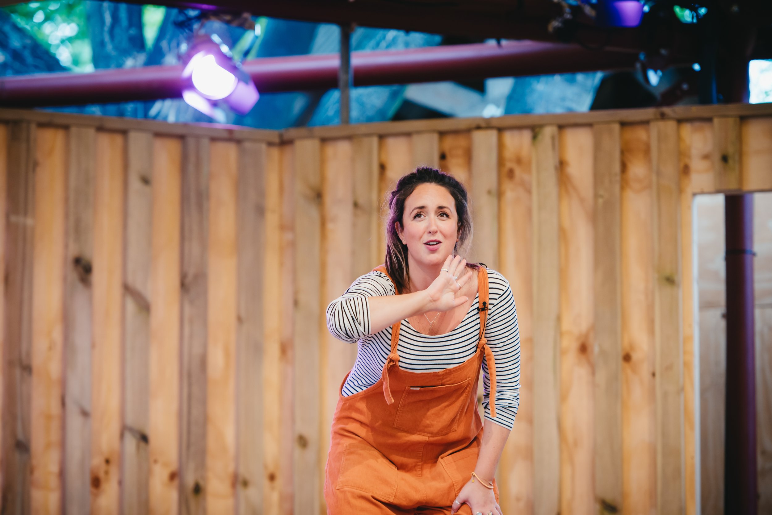 Roann Hassani McCloskey is wearing an orange jumper with black and white striped long sleeve shirt and performs at Globe Theatre