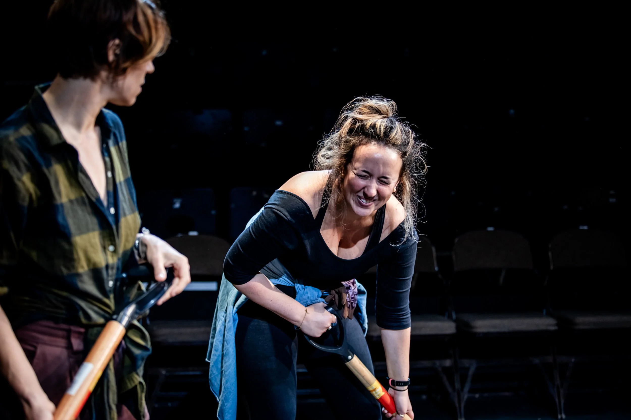 Roann Hassani McCloskey holds a shovel on stage and is bent over laughing