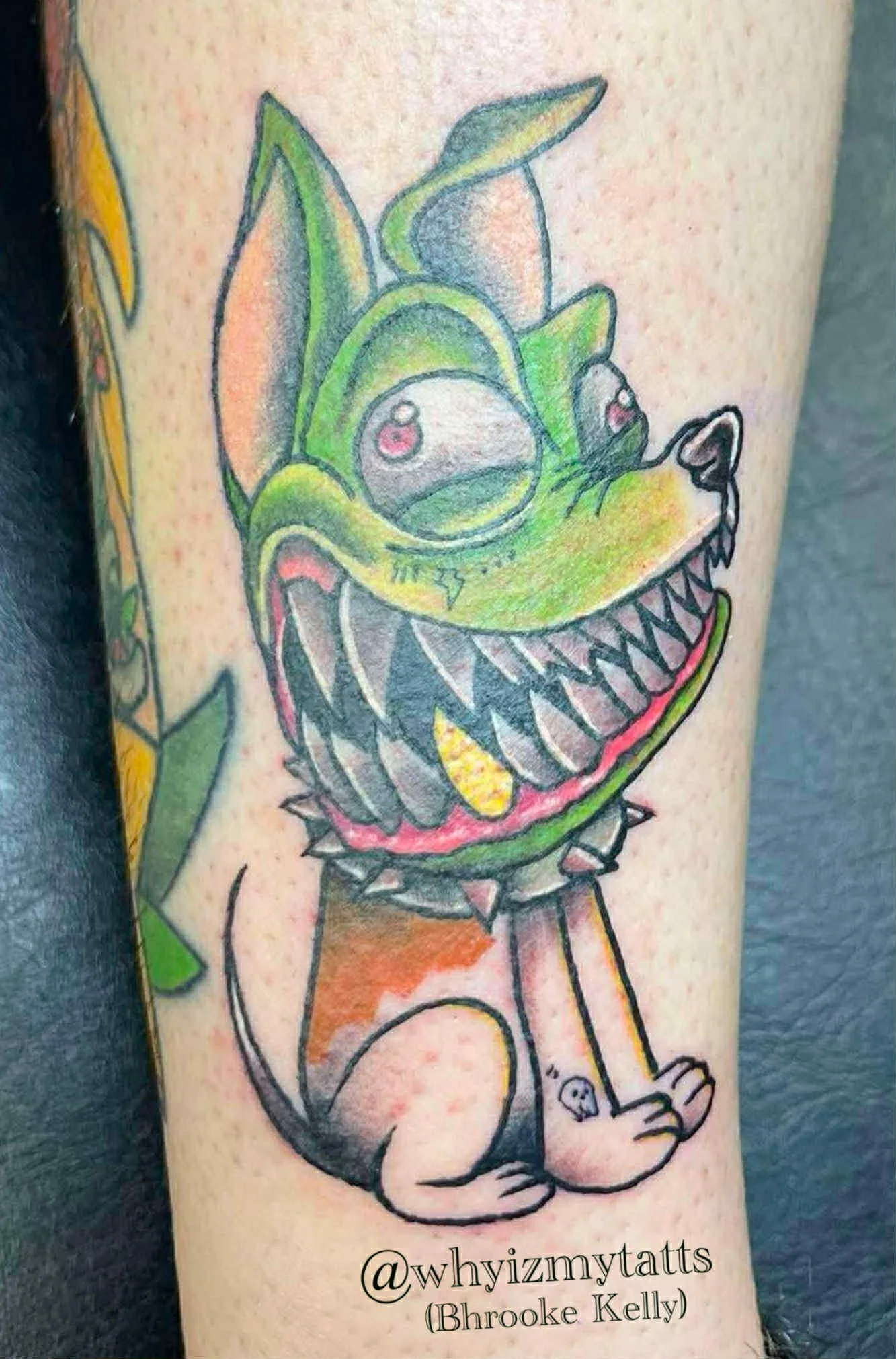 Colorful tattoo of a cartoonish, monstrous dog with multiple eyes, sharp teeth, and spikes around its neck, sitting on its hind legs.