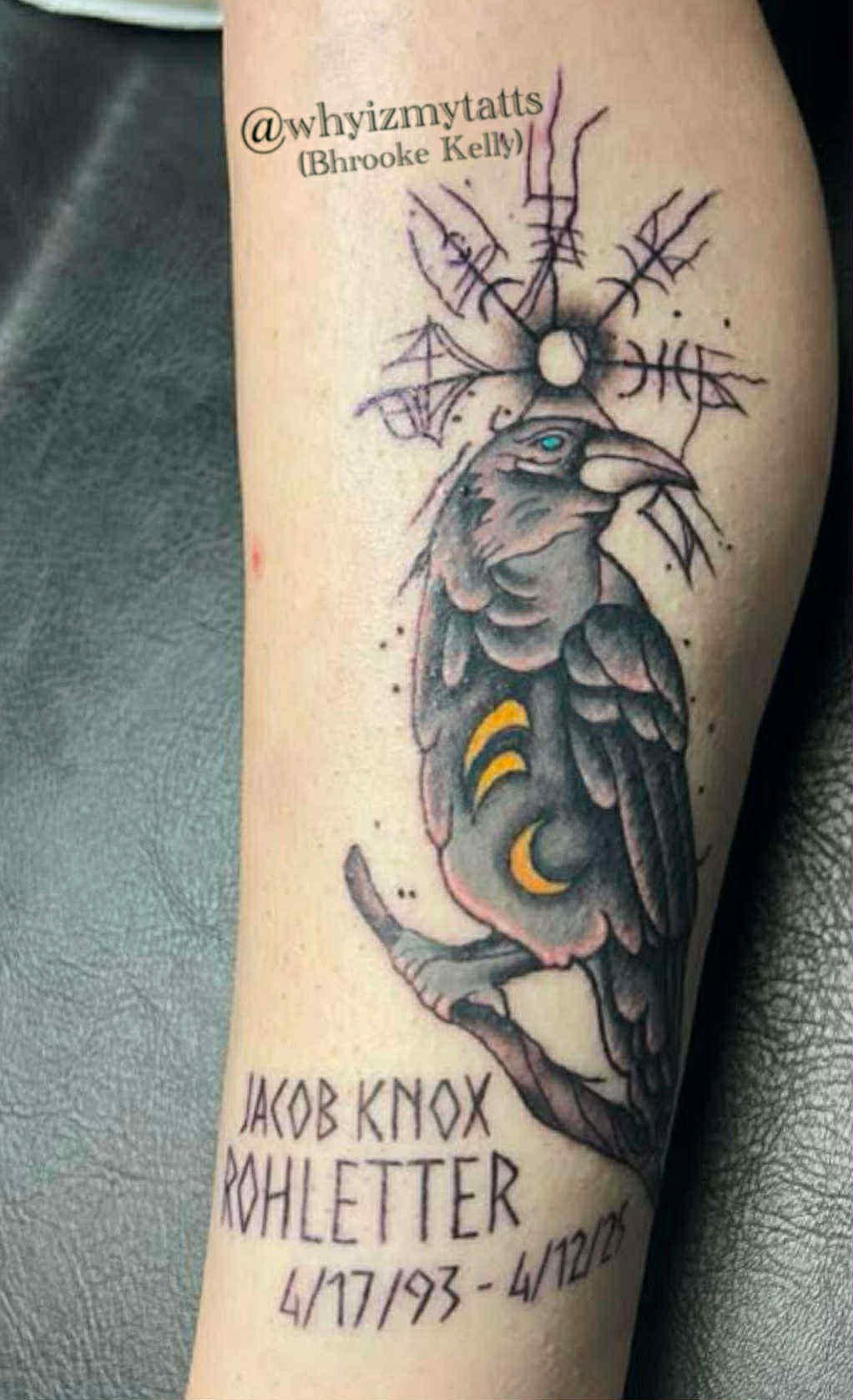 Tattoo of a bird with a spider web above its head, decorated with crescent moons, and text with a social media handle, a name, and a date.