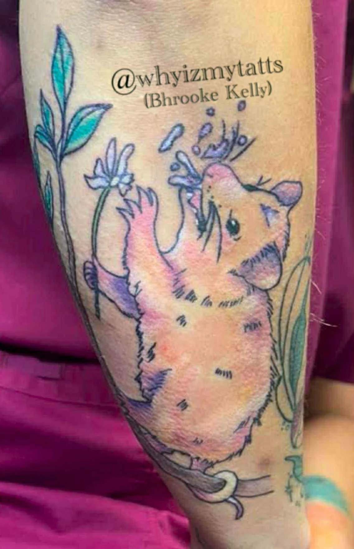 Tattoo of a cartoon-style rat holding a flower on a person's arm, with green leaves surrounding it.