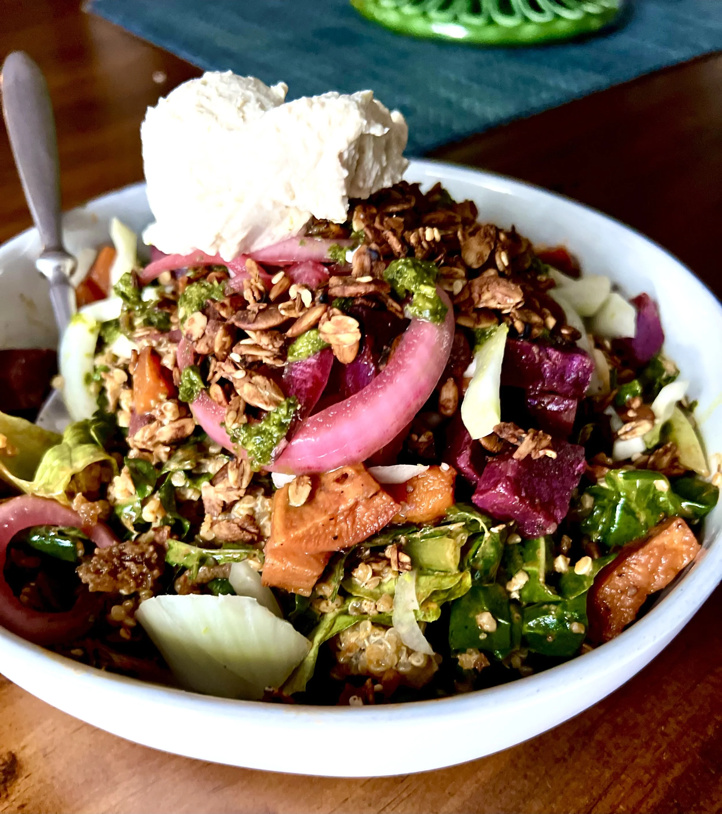 A colorful salad in a white bowl with chopped vegetables, grains, and a dollop of cream or cheese on top.