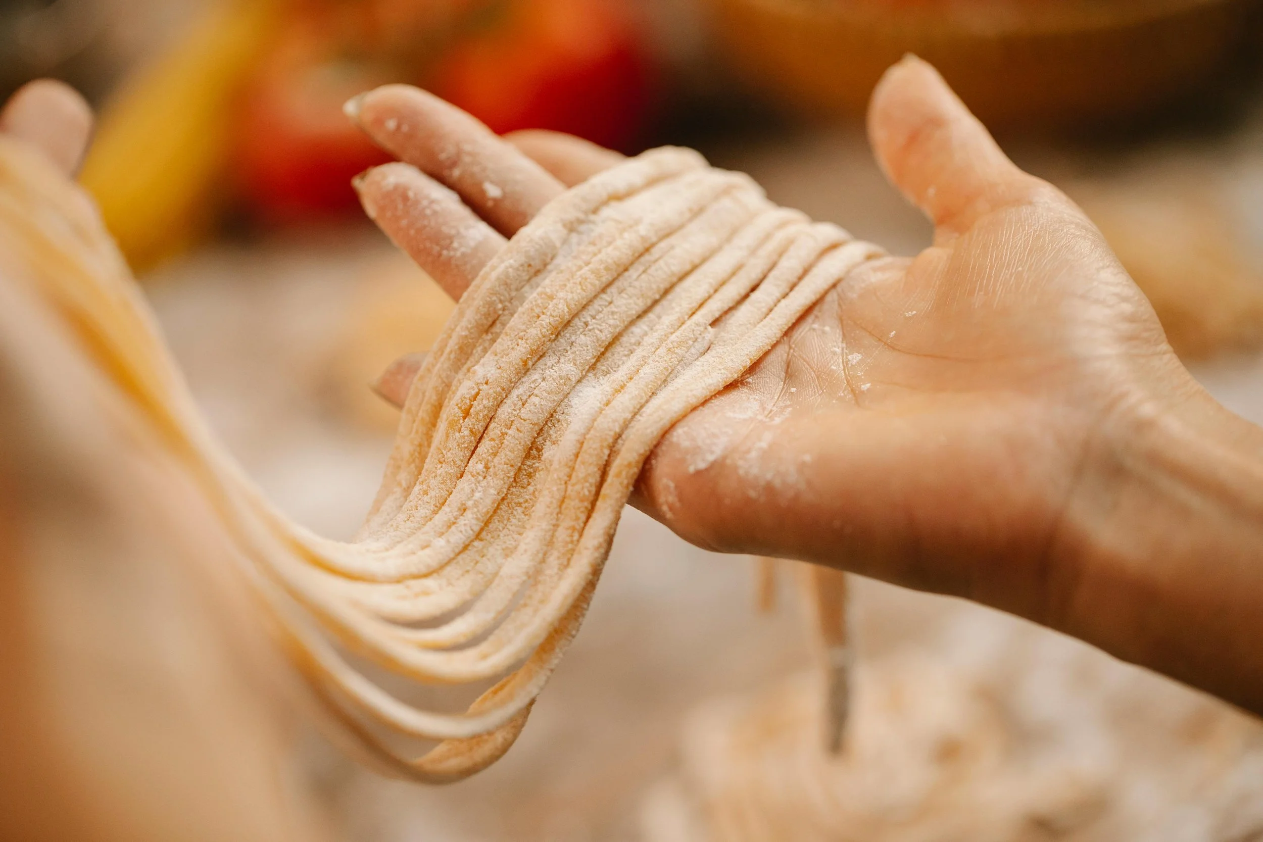 Close-up of a hand holding freshly made pasta noodles, with some flour on the fingers and noodles, in a kitchen setting.
