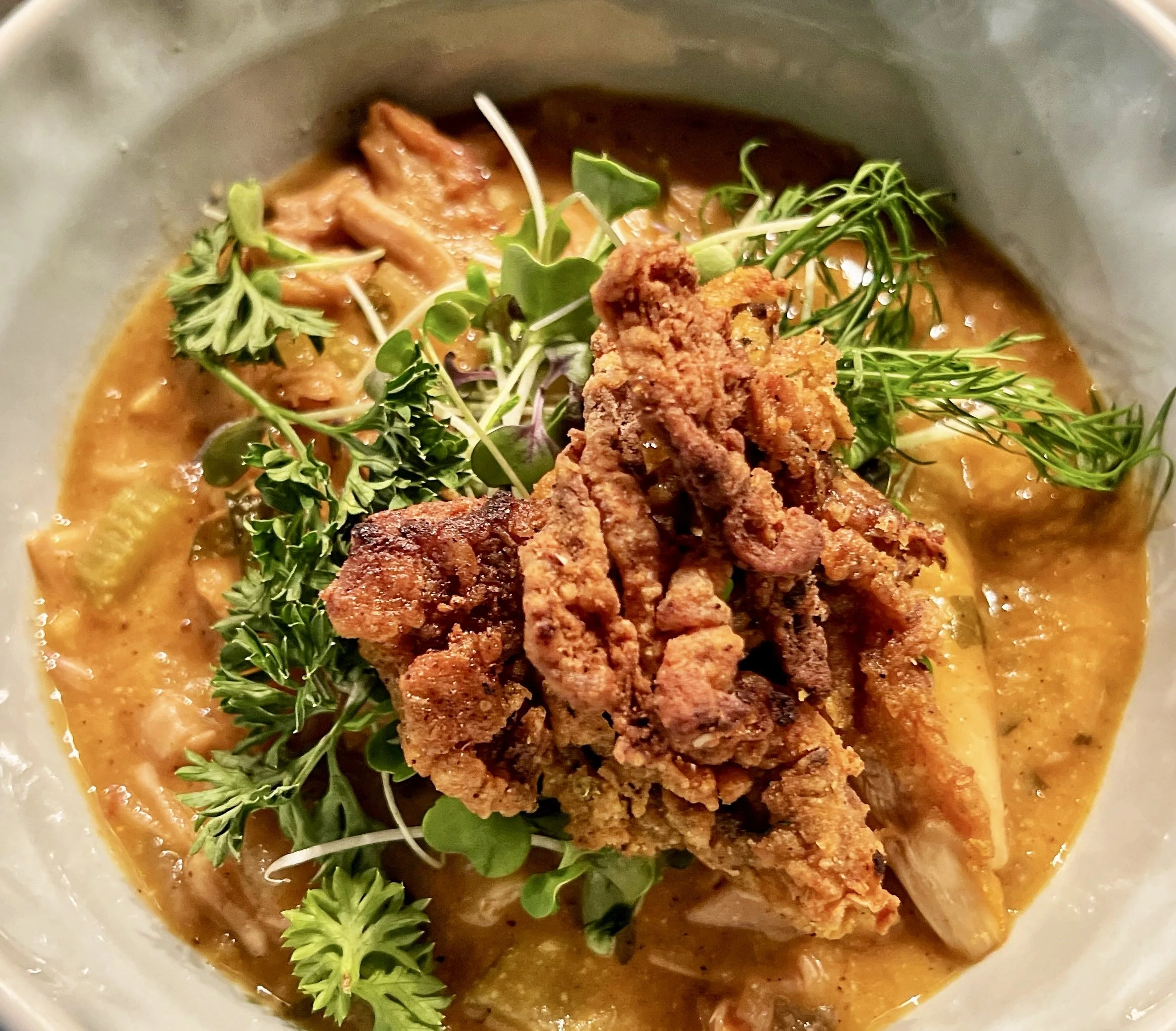 Fried chicken topped with microgreens and herbs in a creamy soup or sauce with vegetables.