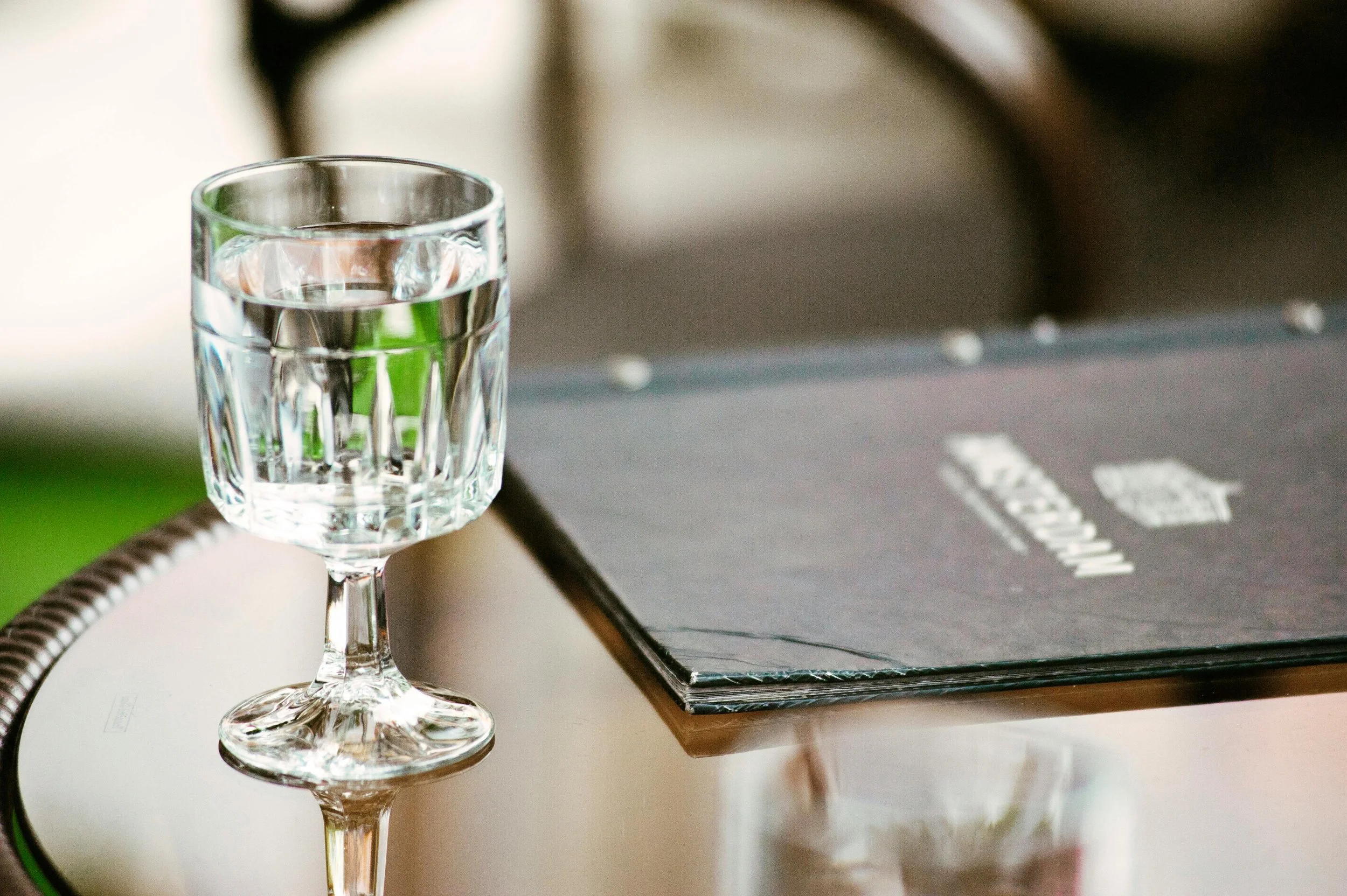 A glass of water on a table with a black menu or notebook nearby