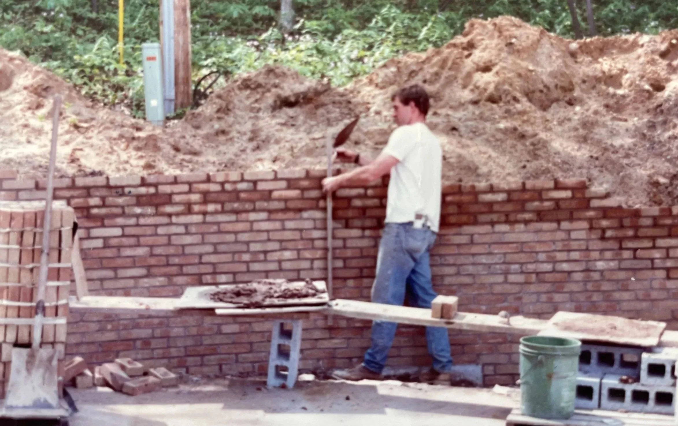 A man working on building a brick wall outdoors, with construction tools and materials around him.