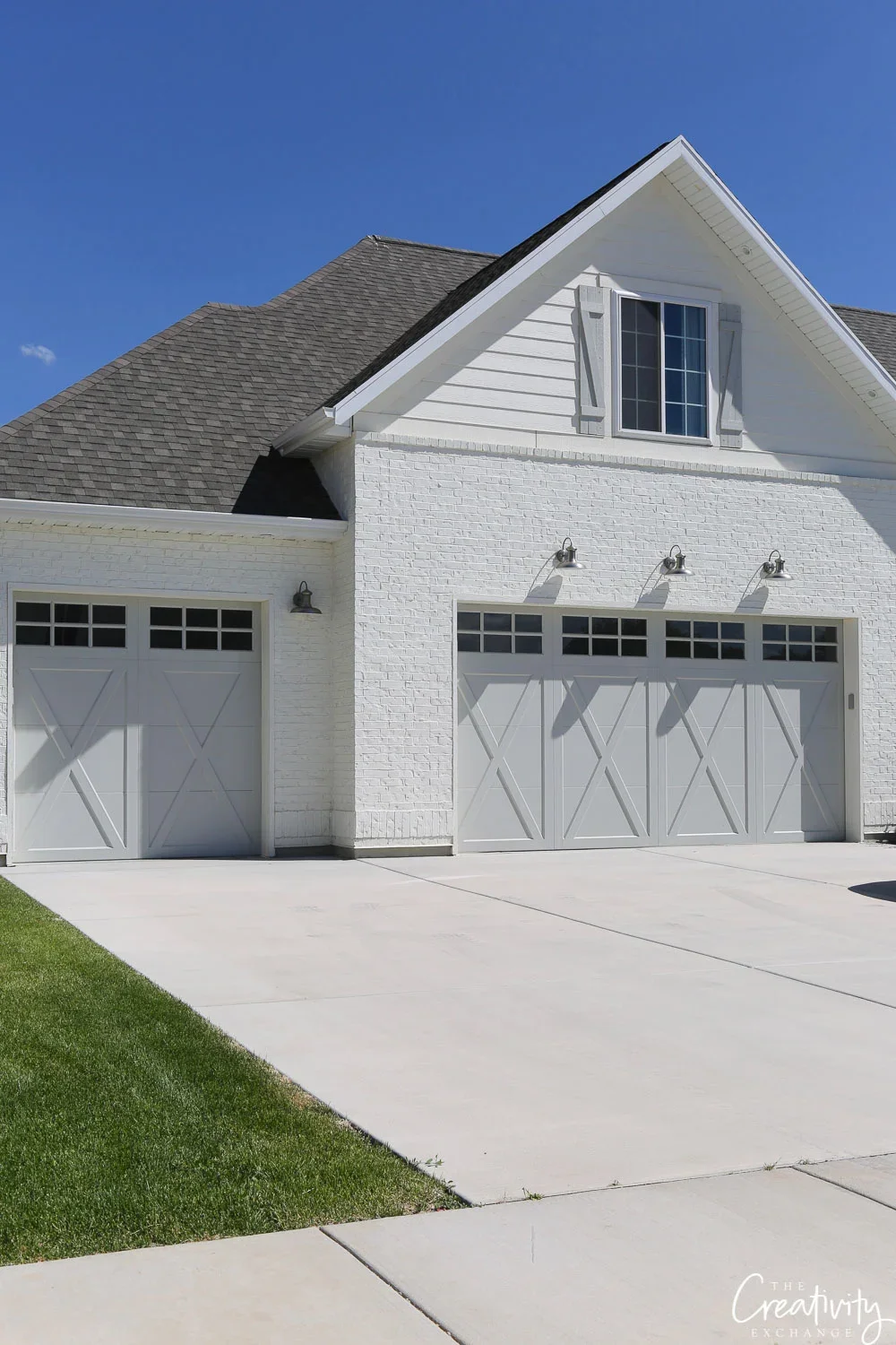 Front view of a white house with two garage doors, decorative lights, and blue sky.