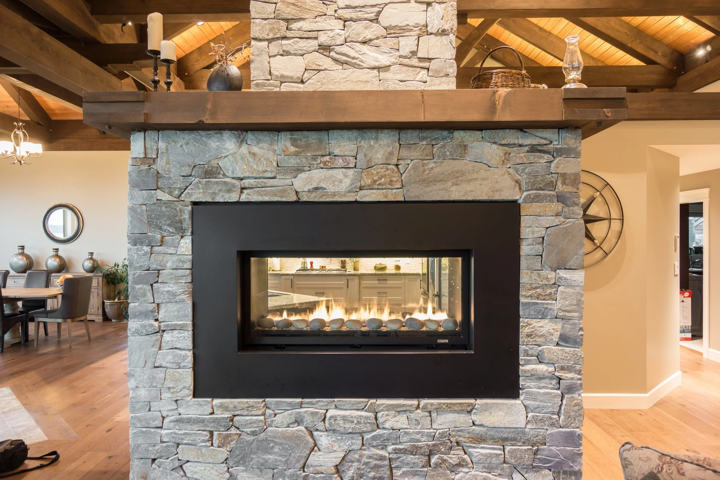 Living room stone fireplace with modern glass gas insert, wooden mantel, and decor on top, in a rustic-style home.