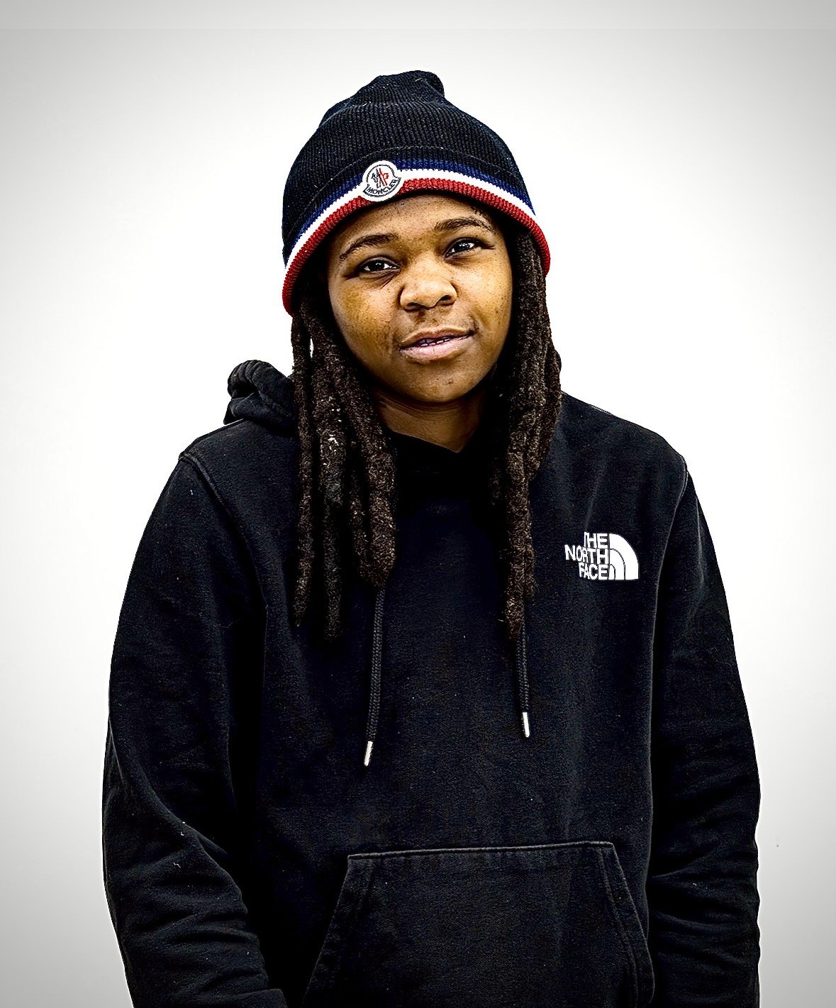 Young person wearing a black The North Face hoodie and a black, red, white, and blue beanie with dreadlocks.