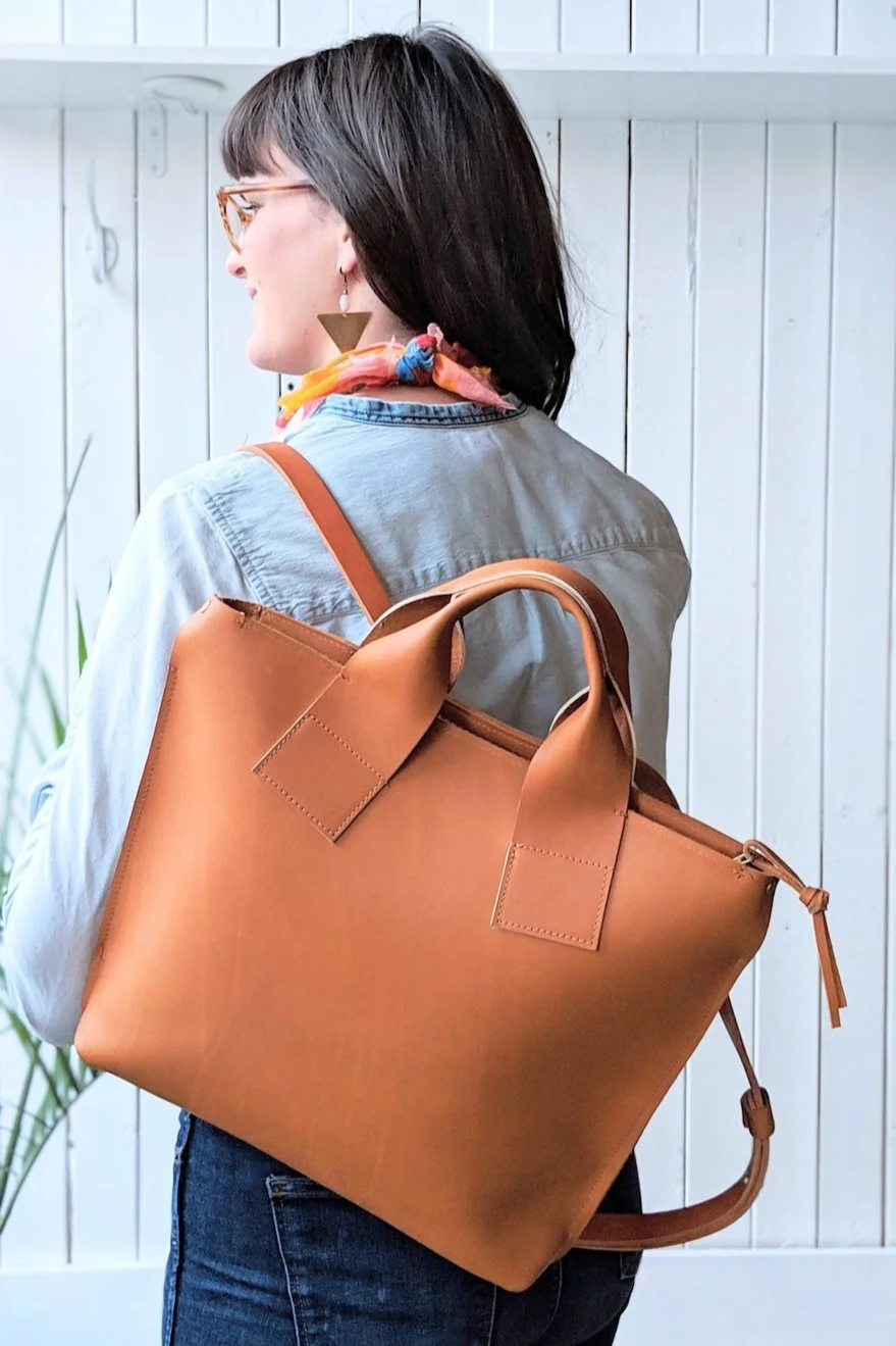 Nicole Parker modeling a tan leather backpack and looking away from the camera with my back to the photo
