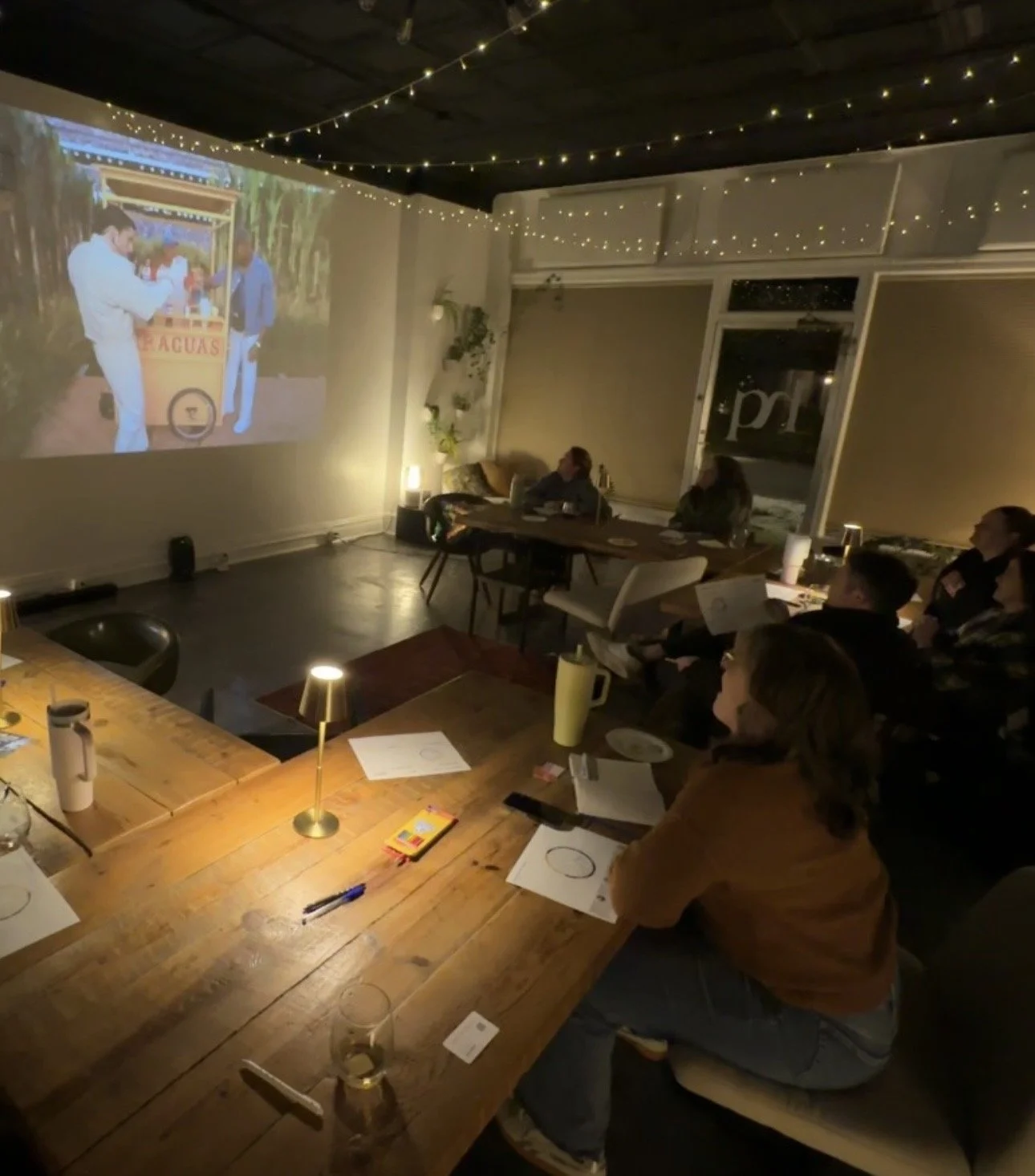 Small business owners are gathered around an l-shaped table, facing a projector of the super bowl. In front of them is a worksheet for business planning and strategies