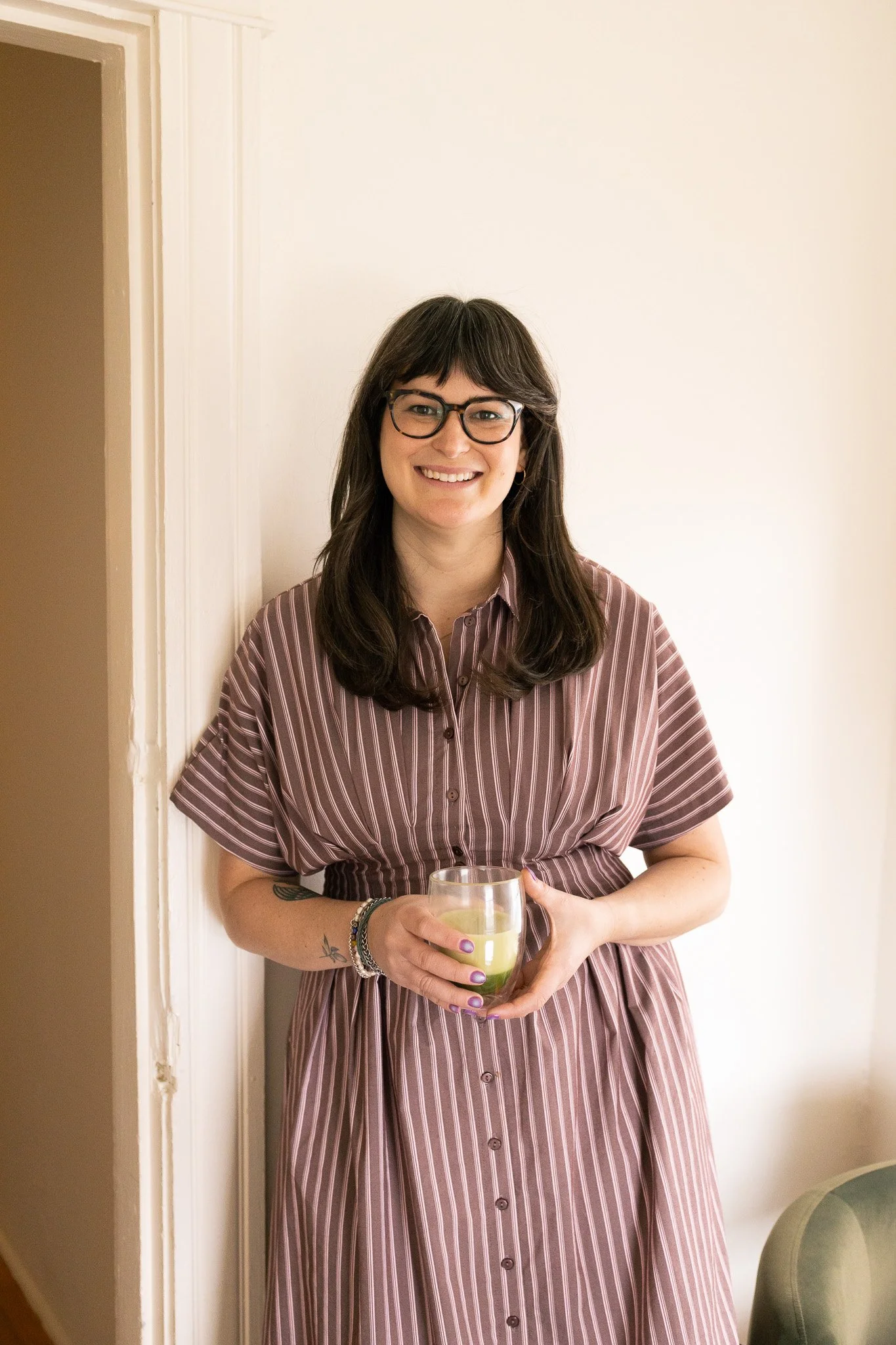 Nicole Parker standing against a wall holding a cup of Matcha, smiling and looking straight ahead