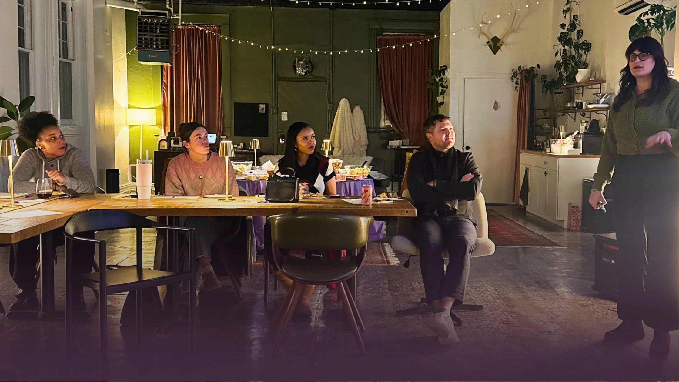 Nicole Parker is standing, speaking to a group of seated small business owners in a dark, cozy co-working venue. Lights are dim and it is evening