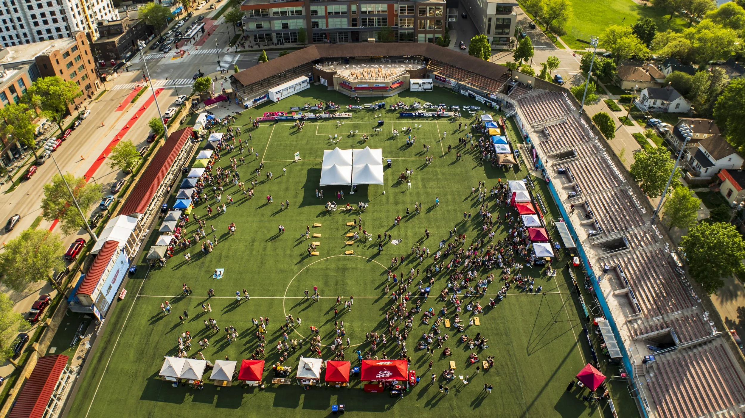 An aerial view of a sports stadium during an outdoor event with tents, crowds, and surrounding buildings.