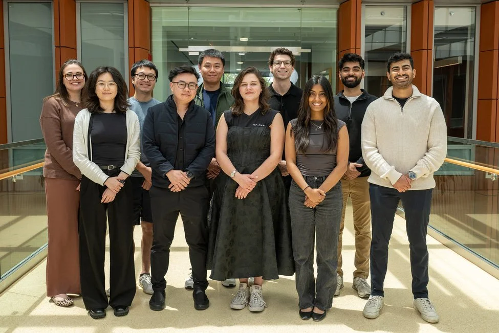 A diverse group of ten young adults standing together in a modern indoor setting, smiling for the camera.
