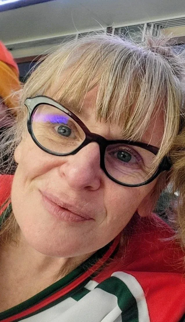 A woman with blonde hair wearing glasses, smiling at the camera, dressed in a New Jersey Devils hockey jersey.