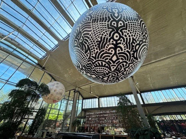 A room with a glass ceiling. There are two large spherical objects hanging from it. One black and white with a patter, the other white and black with a pattern. 