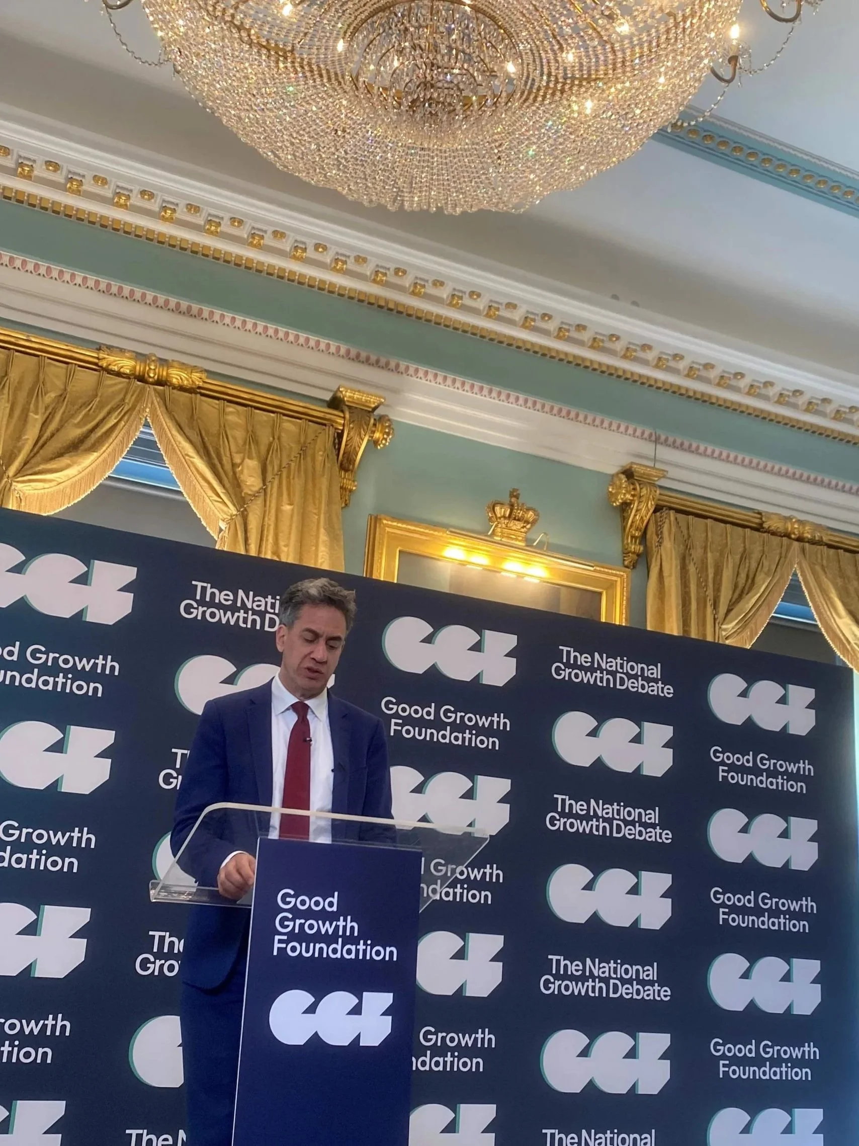A picture of Ed Milliband standing at a lectern in front of a banner with a purple background with the Good Growth Foundation and the National Growth Debate written on it