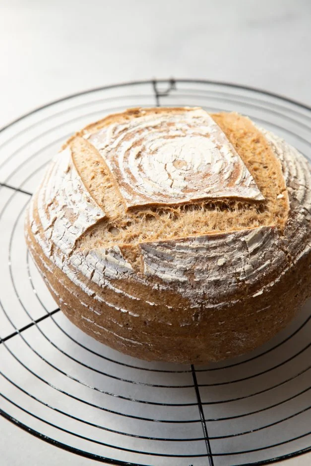 Pão de fermentação natural sobre uma grade de resfriamento, com uma crosta rústica e uma pontuação no topo.