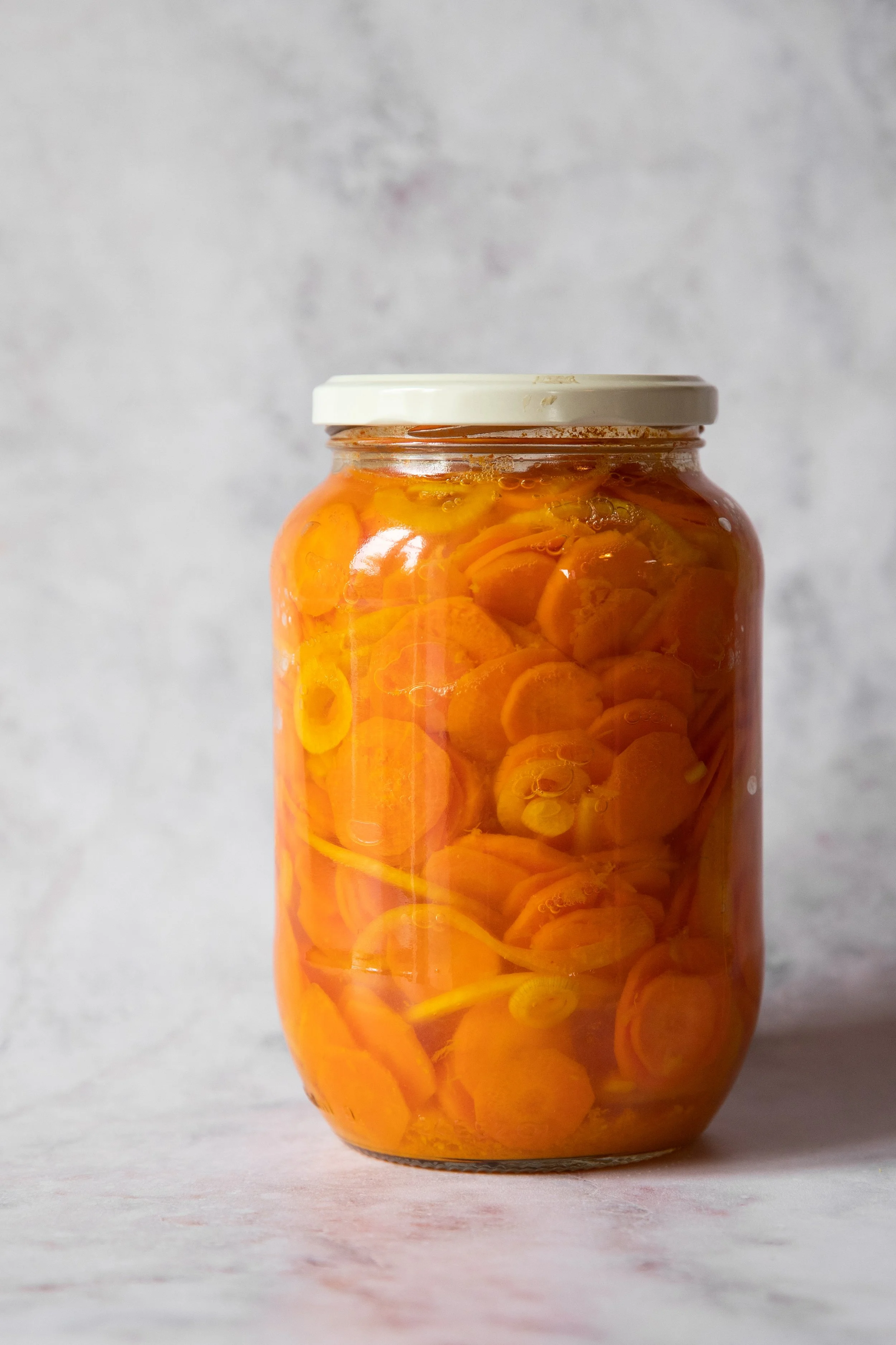 Pote de vidro com pimentas amarelas em conserva e tampa branca.