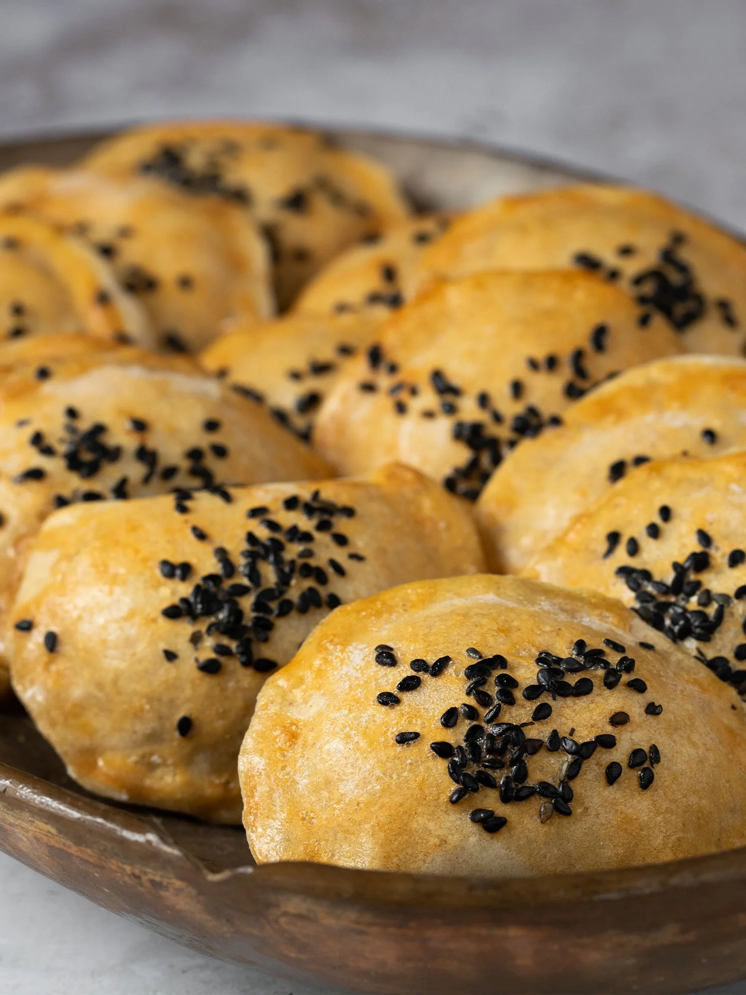 Pãezinhos dourados com gergelim preto em um prato rústico.