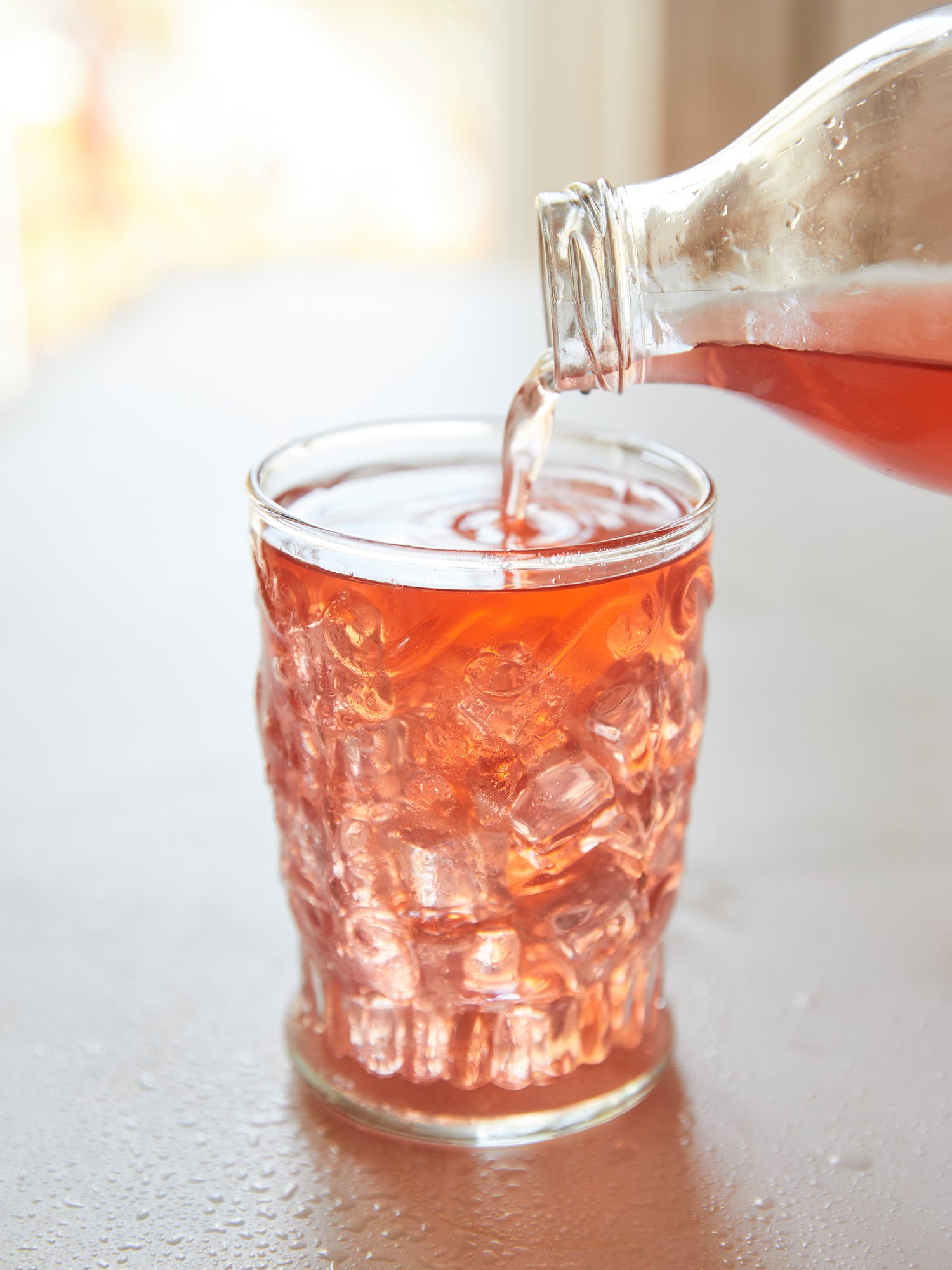 Garrafa de vidro a despejar uma bebida colorida e refrescante para um copo com gelo.