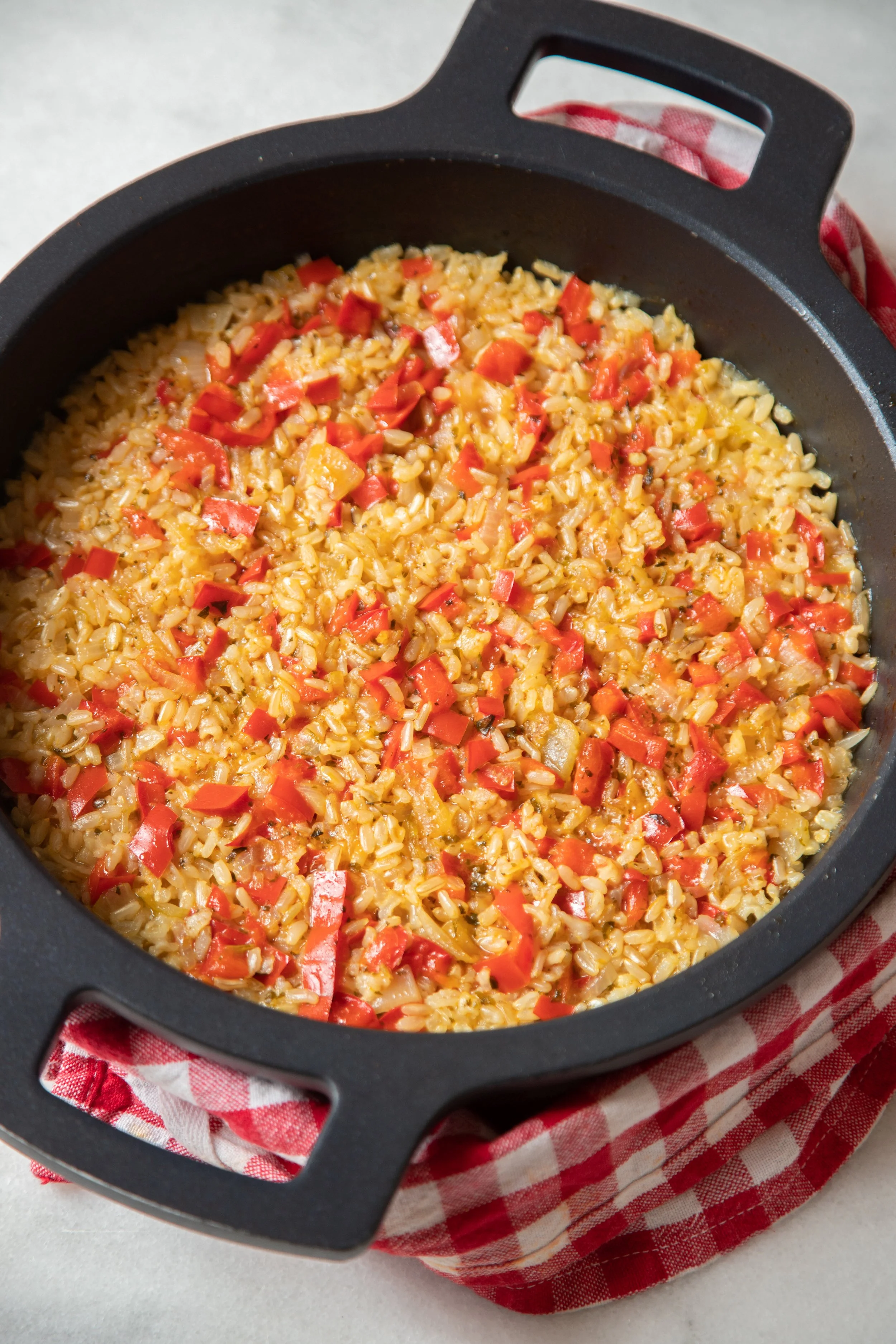 Arroz cozido com pimentões vermelhos em uma panela preta.