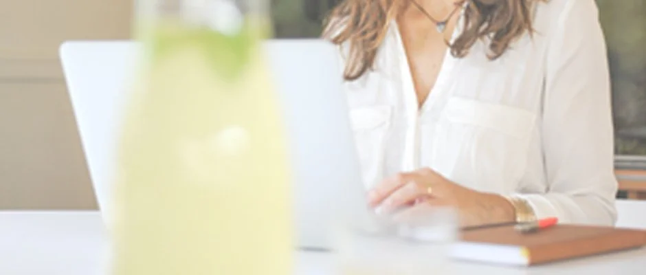 Pessoa usando um laptop em uma mesa de escritório, com uma planta desenfadada no primeiro plano.