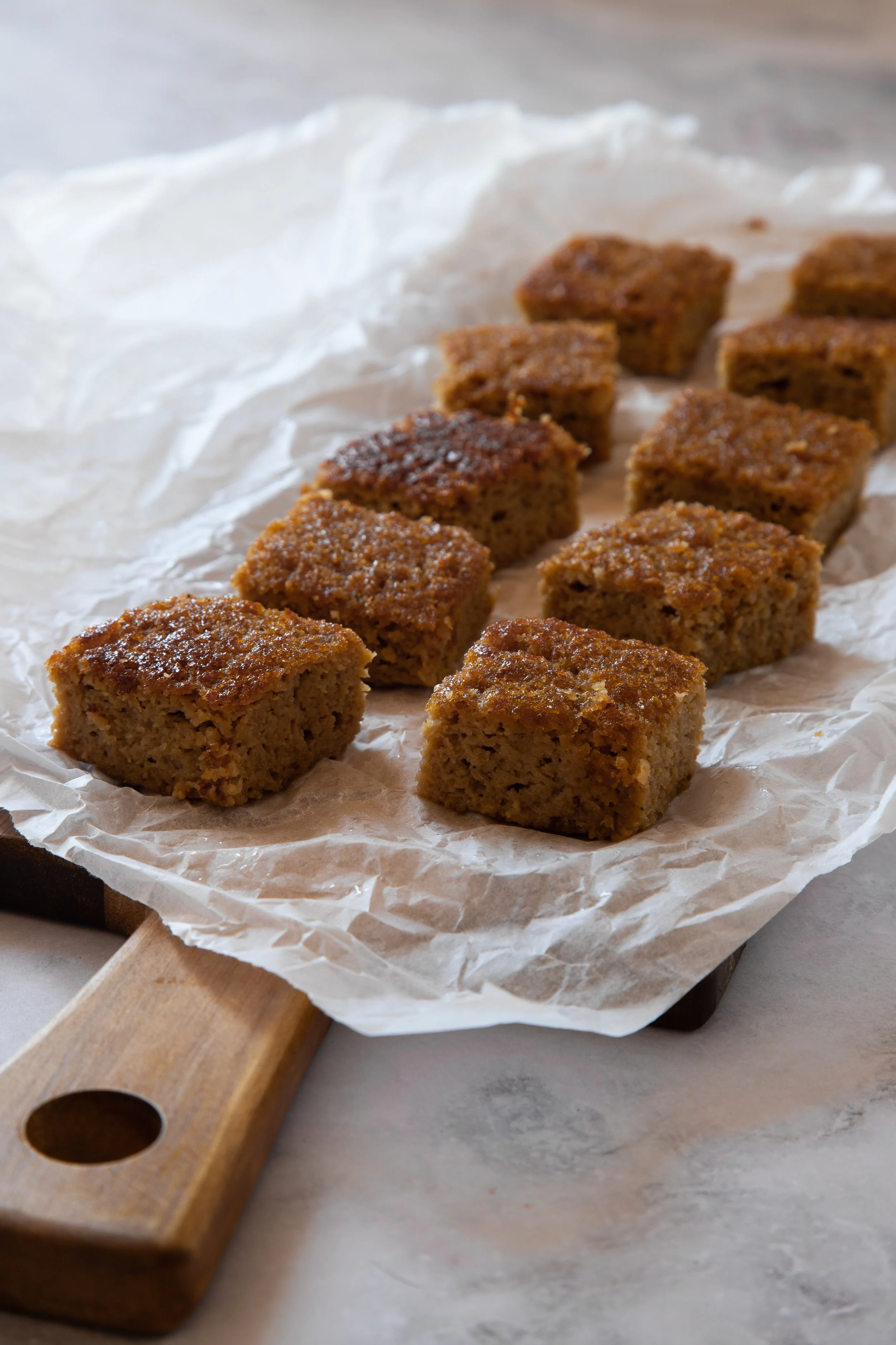 Cubos de bolo de banana assados sobre papel manteiga em uma tábua de madeira.