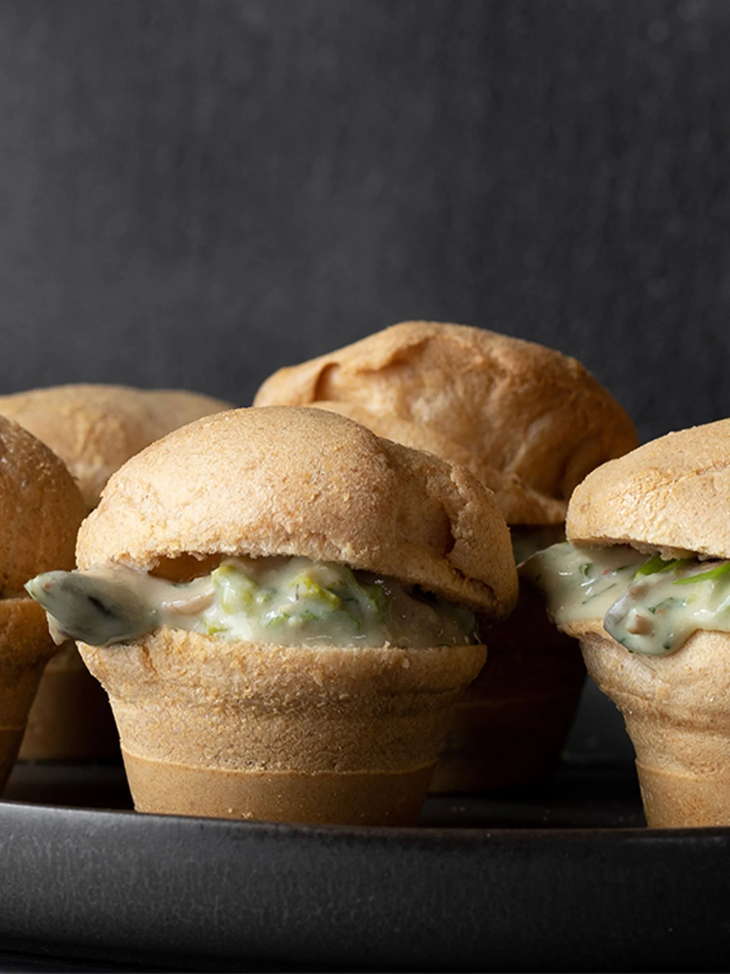 Mini quiches com recheio de queijo e ervas, em uma travessa preta.