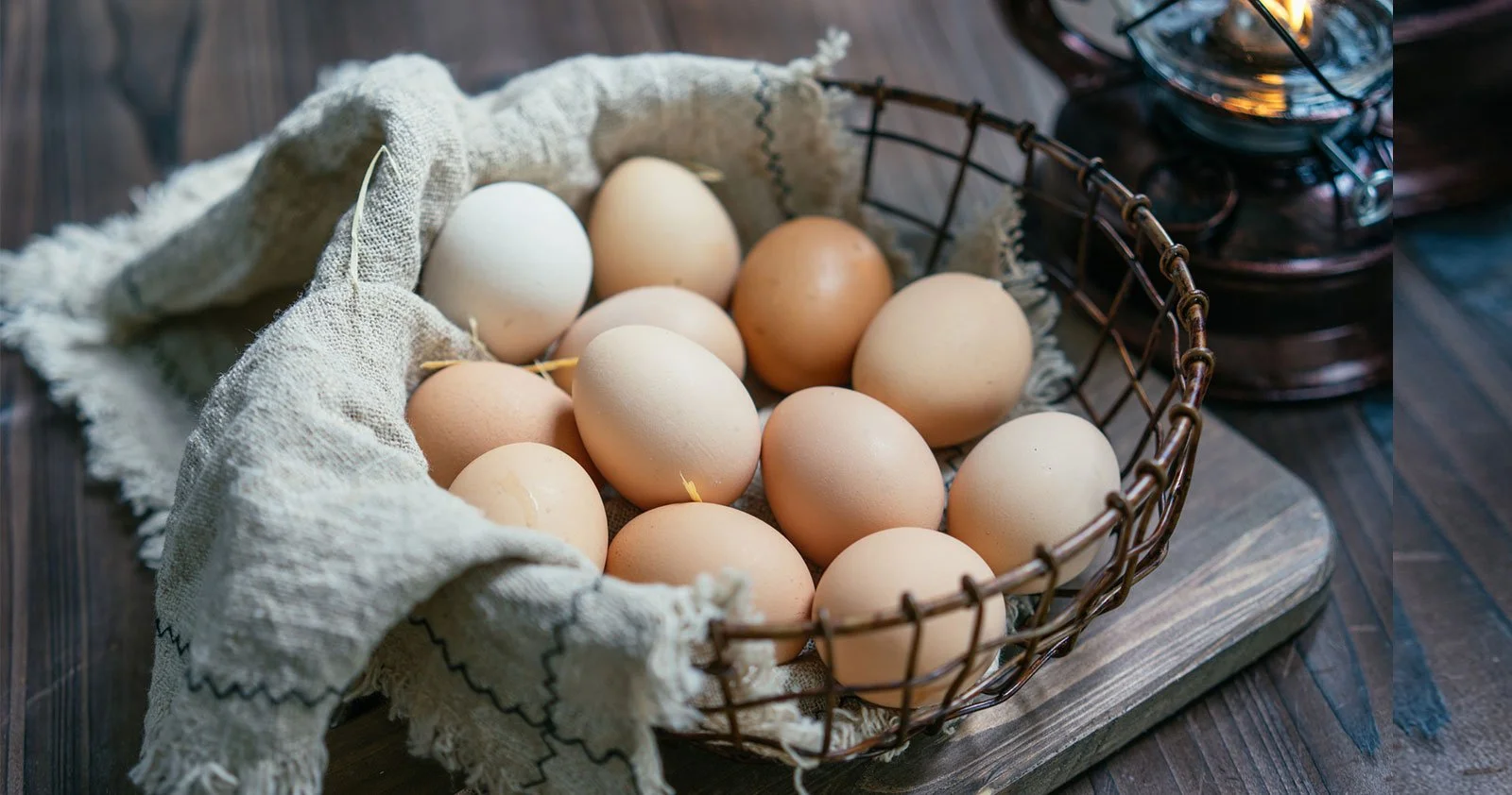 Cesta com ovos de galinha de cores claras sobre uma tábua de madeira