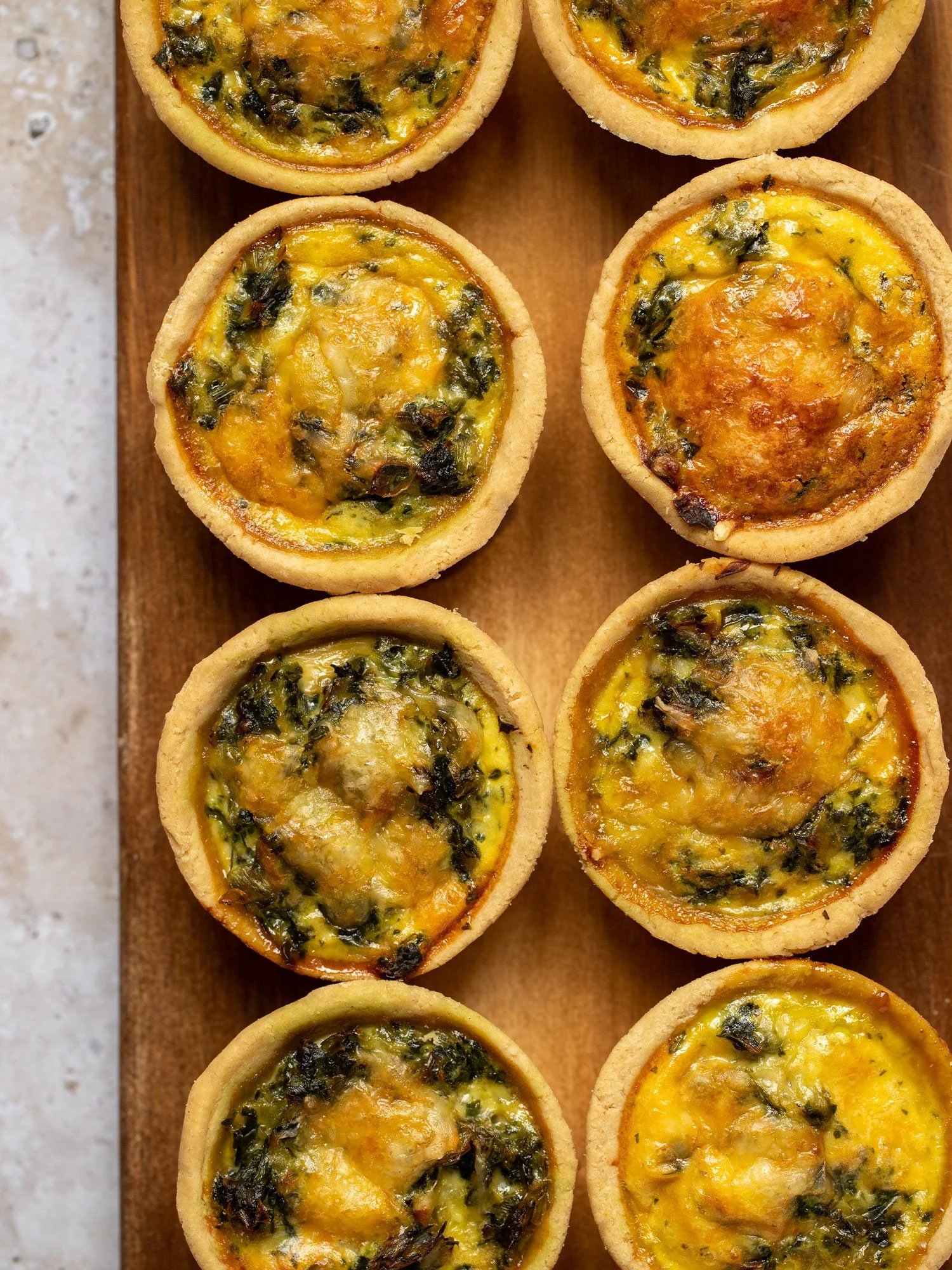Tortinhas de queijo com recheio de espinafre e ervas, assadas, dispostas sobre uma tábua de madeira.