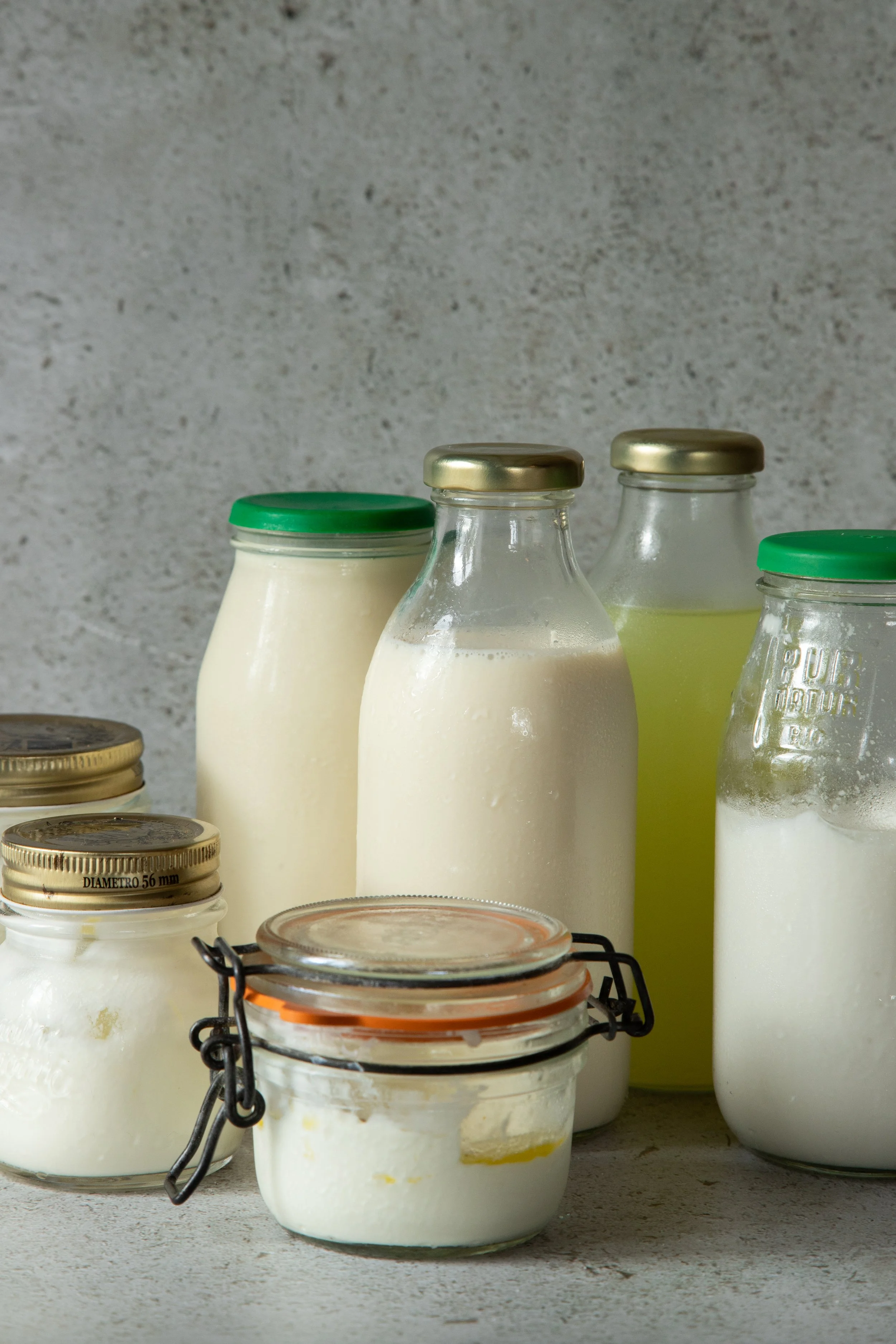 Vários potes de vidro com produtos lácteos, como iogurte e leite, sobre uma superfície de piso