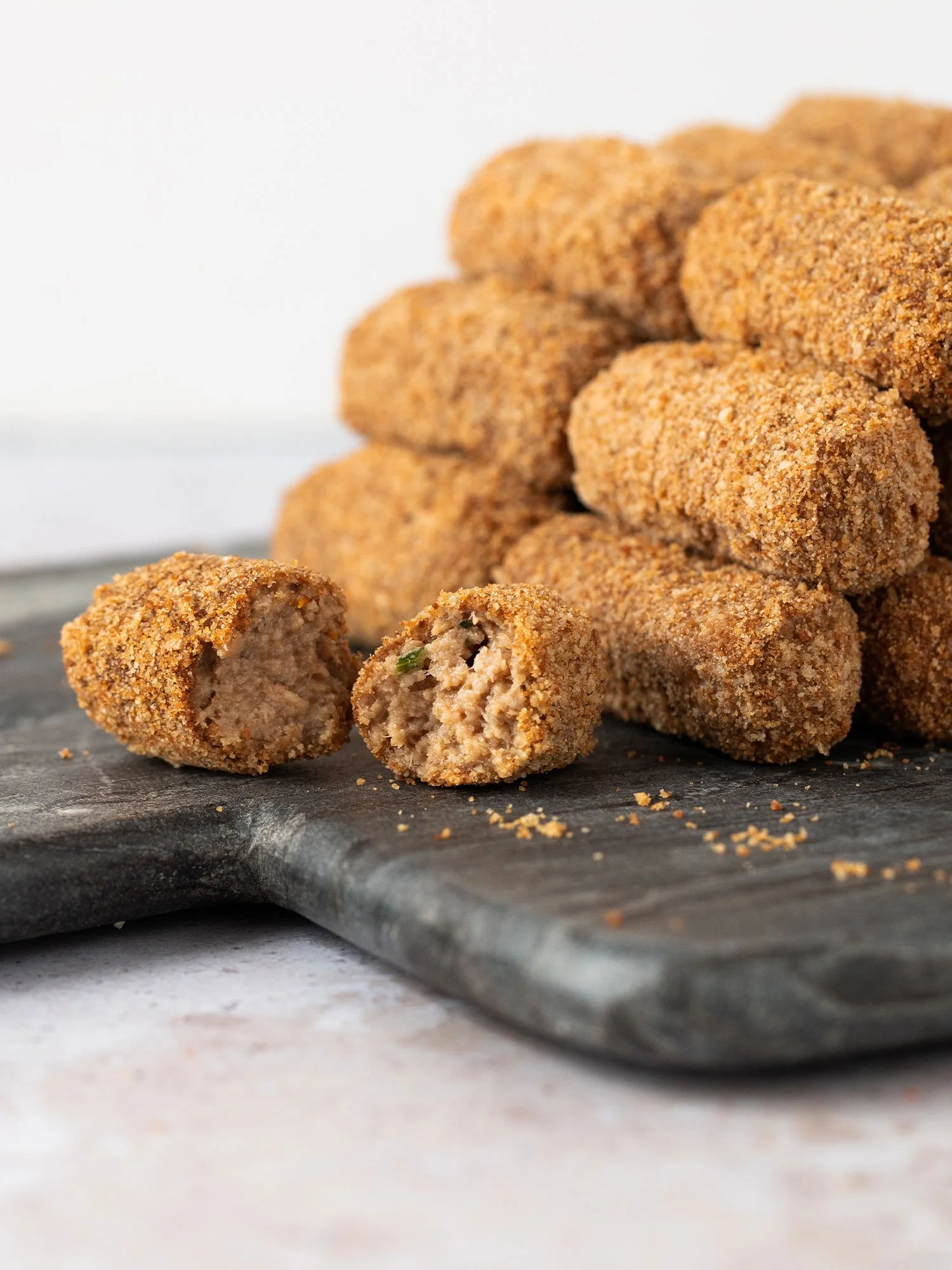 Croquetes empanados em uma tábua de pedra, um deles cortado ao meio revelando o recheio