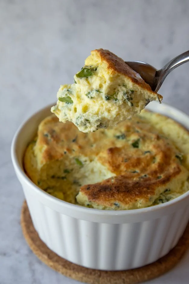 Feijoada de queijo com pedaços de queijo derretido e ervas, em uma tigela branca com uma colher de metal.