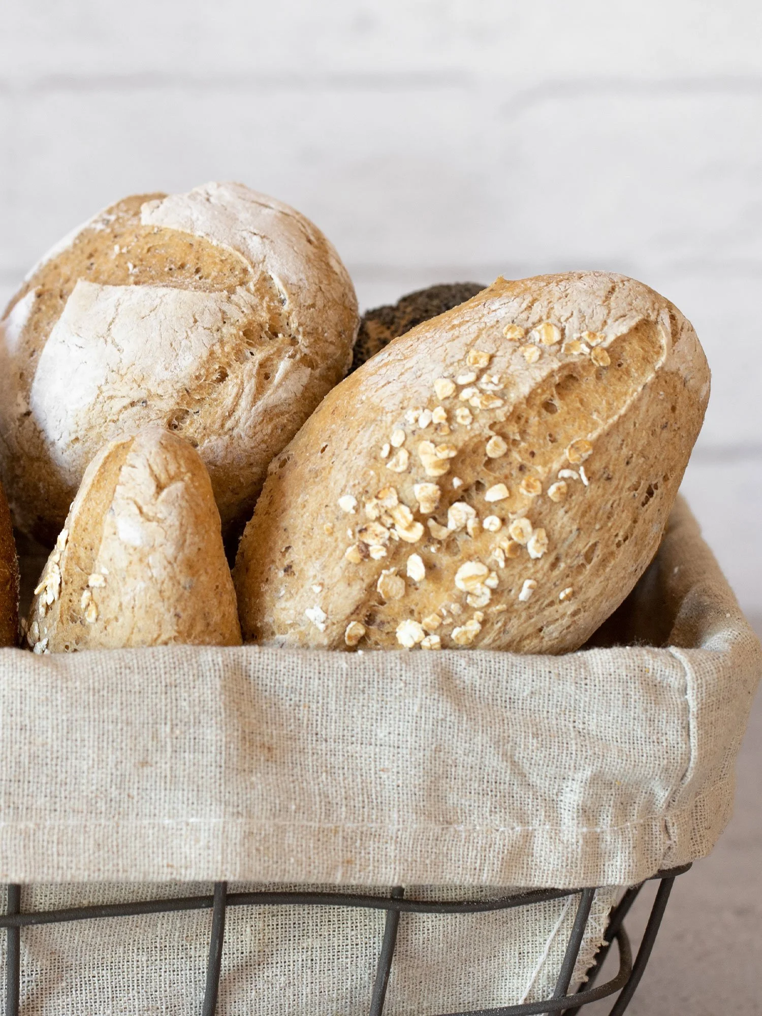 Cesta com pães variados, alguns cobertos com aveia. Fundo branco.