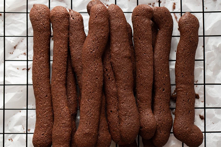 Biscoitos de chocolate alongados e de formato irregular sobre uma grade de arame.