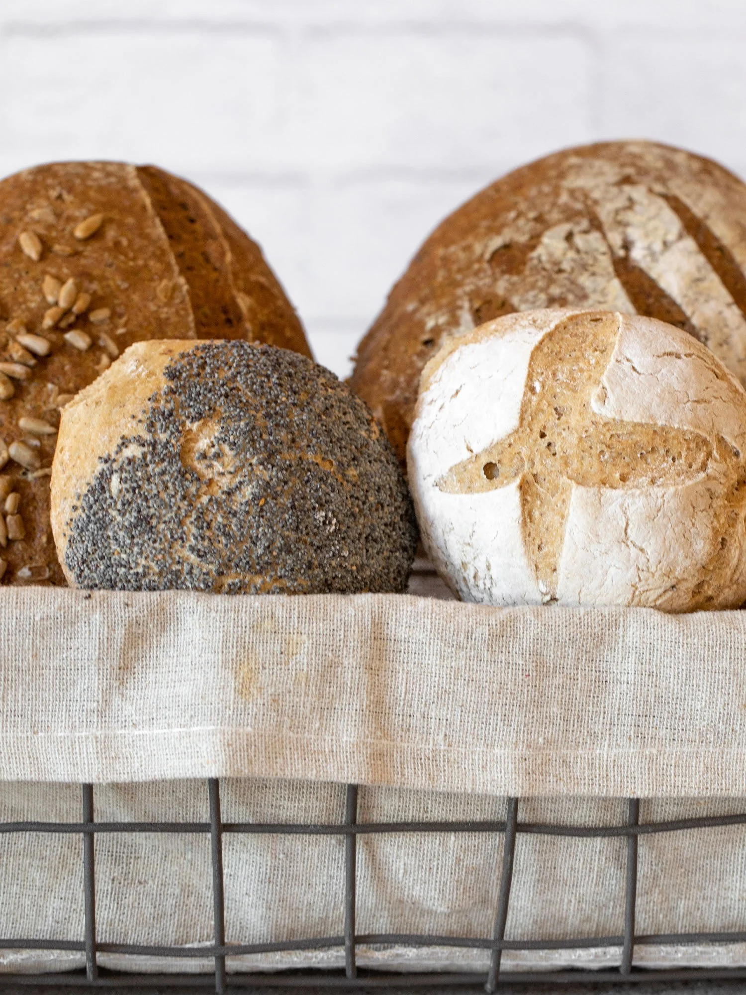 Tres pães artesanais com diferentes coberturas e incrustações, colocados em uma cesta com um pano branco.