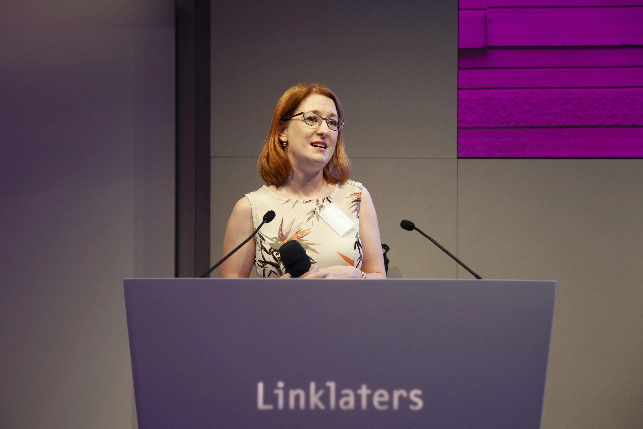 Charity speaker Diana Squires stands by a purple podium and microphone with the Linklaters logo. Diana lectures about innovation and problem-solving at a World Environment Day event in London.