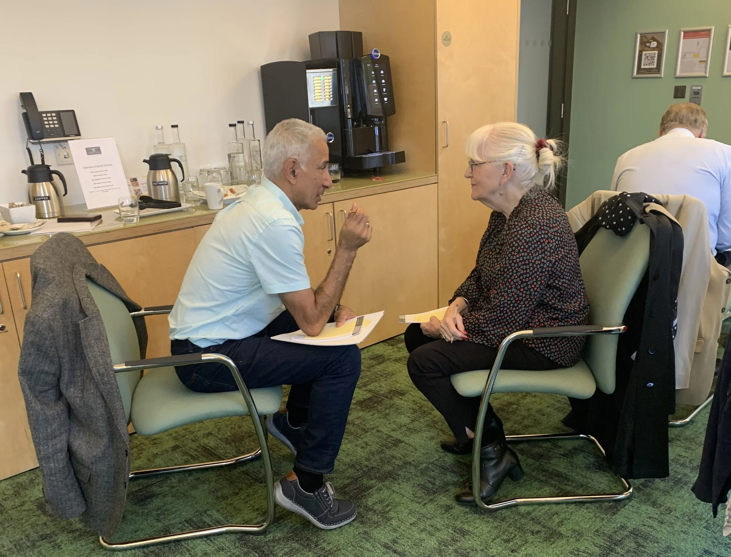 A male and female charity trustee face each other in chairs, their knees almost touching as they engage in a Board Away Day designed and facilitated by Diana Squires. They have open body language and are listening actively.