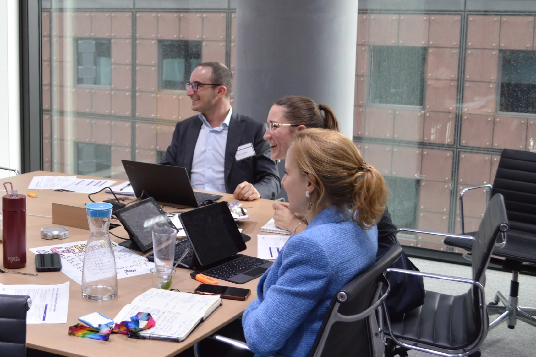 To illustrate the consulting work Diana Squires supported for NSPCC, this picture shows 3 business consultants Diana worked with to develop strategic recommendations. One man and two women laugh and collaborate with notebooks and pens.