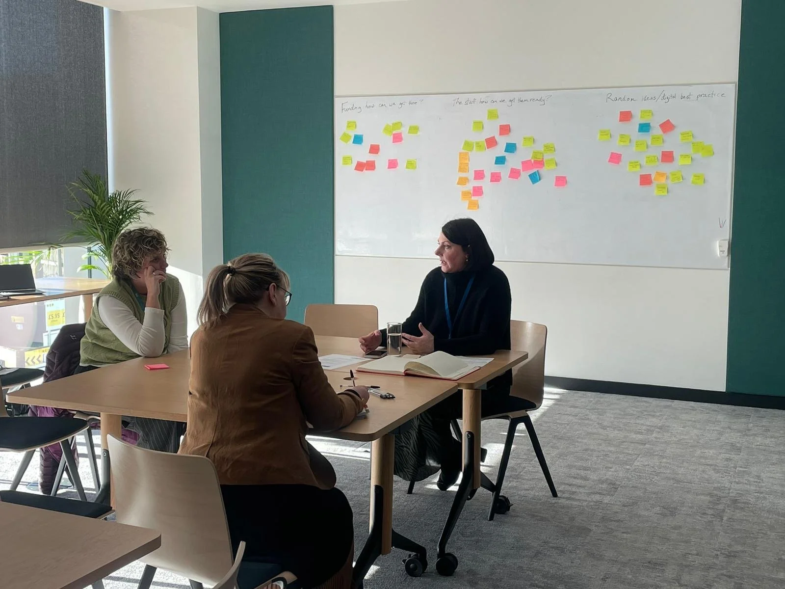 Three brunette business women sit in front of a post-it idea generation board. They are brainstorming strategies at a creative problem-solving event that facilitator Diana Squires organised for Scotland’s SAMH charity.