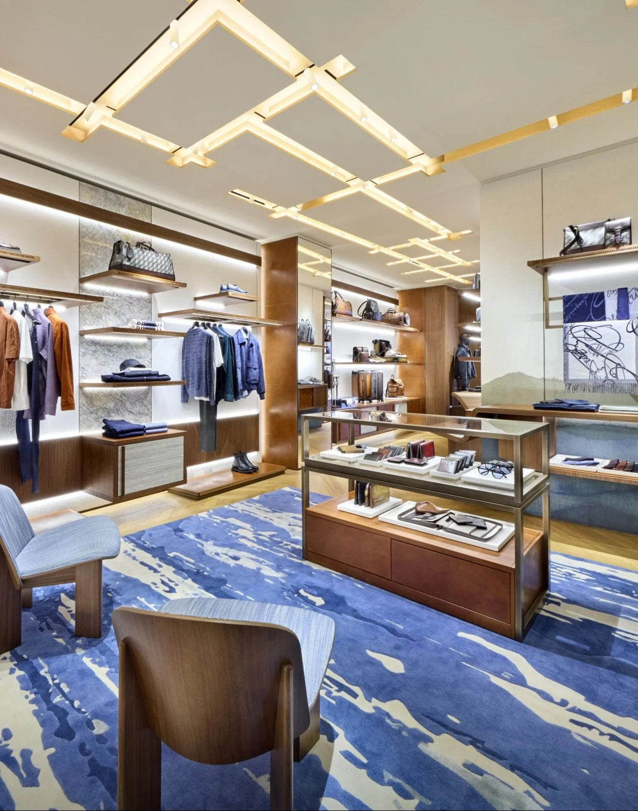 Intérieur d'une boutique de mode élégante avec vêtements, sacs et accessoires exposés sur des étagères en bois, un sol recouvert d'un tapis bleu et des meubles en bois.